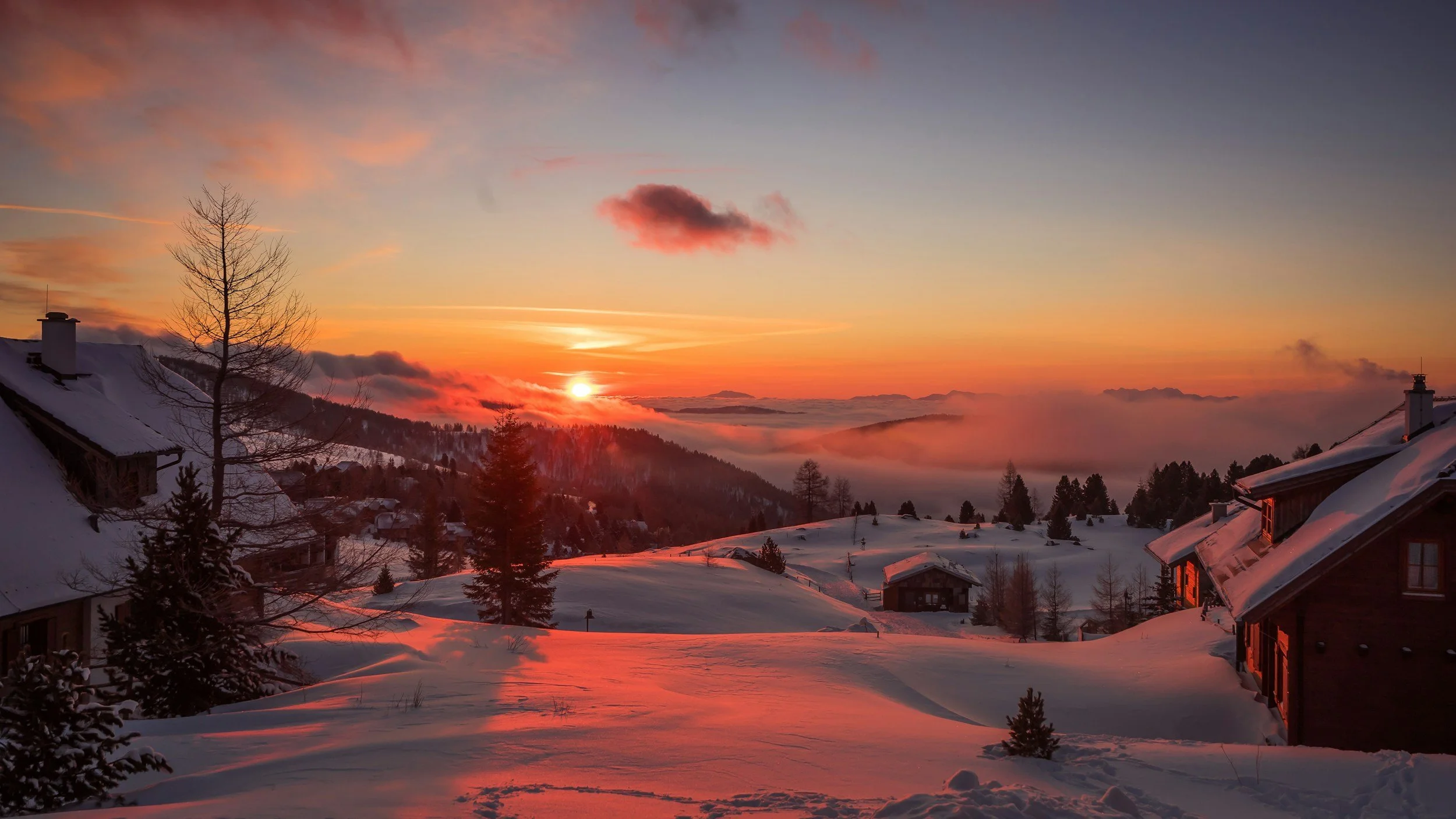 Sunset over snow-covered houses and mountains with a colorful sky and clouds.