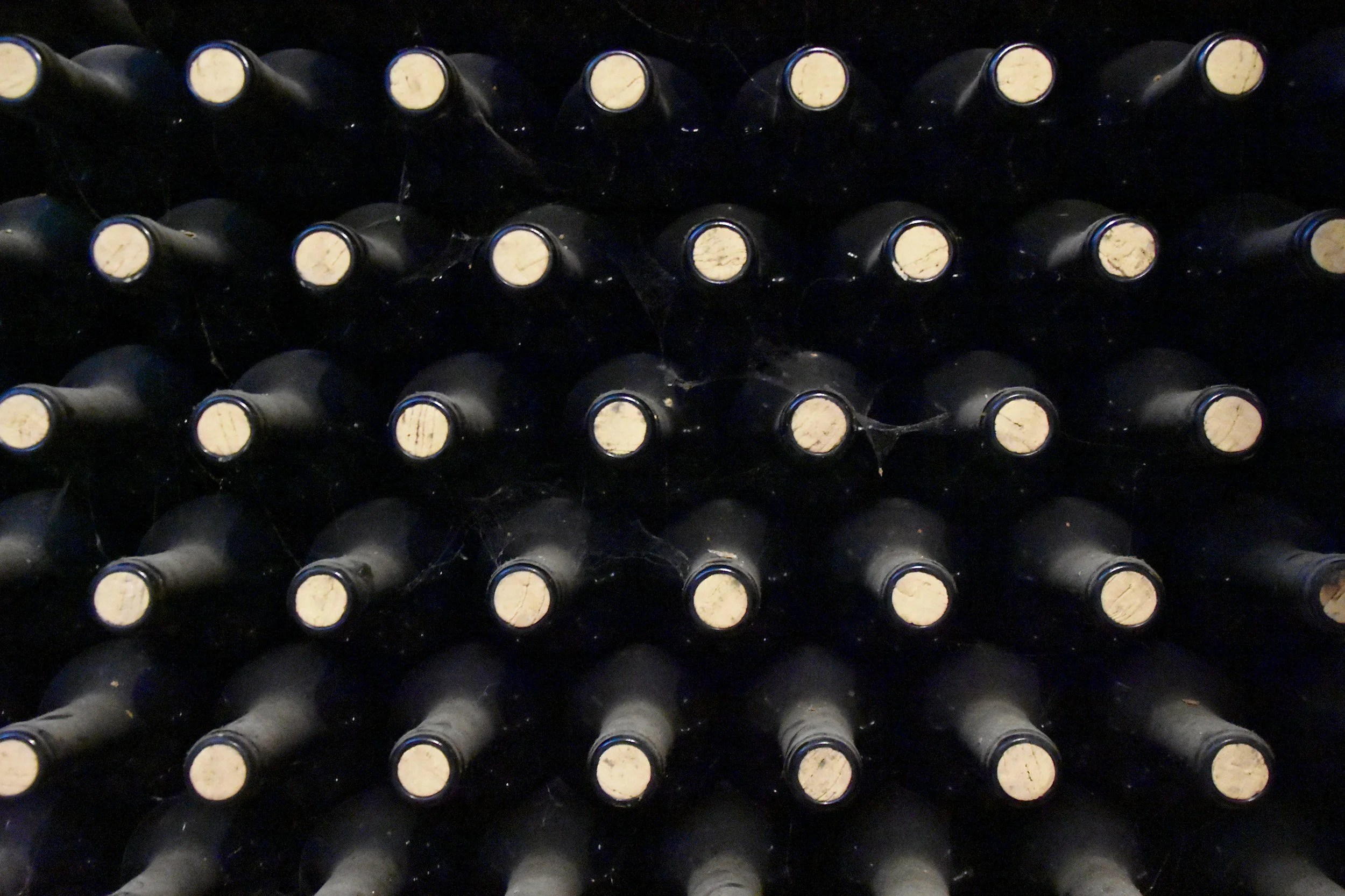 A collection of wine bottles laid horizontally in a wine rack, with their corks facing upward.