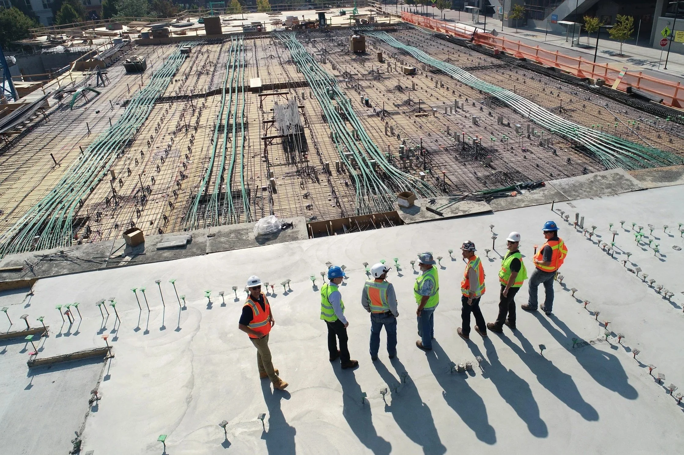Construction workers wearing safety vests and helmets inspecting a building site with exposed reinforcement steel and ongoing concrete work.