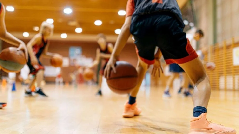 Children practicing basketball drills in an indoor gymnasium.