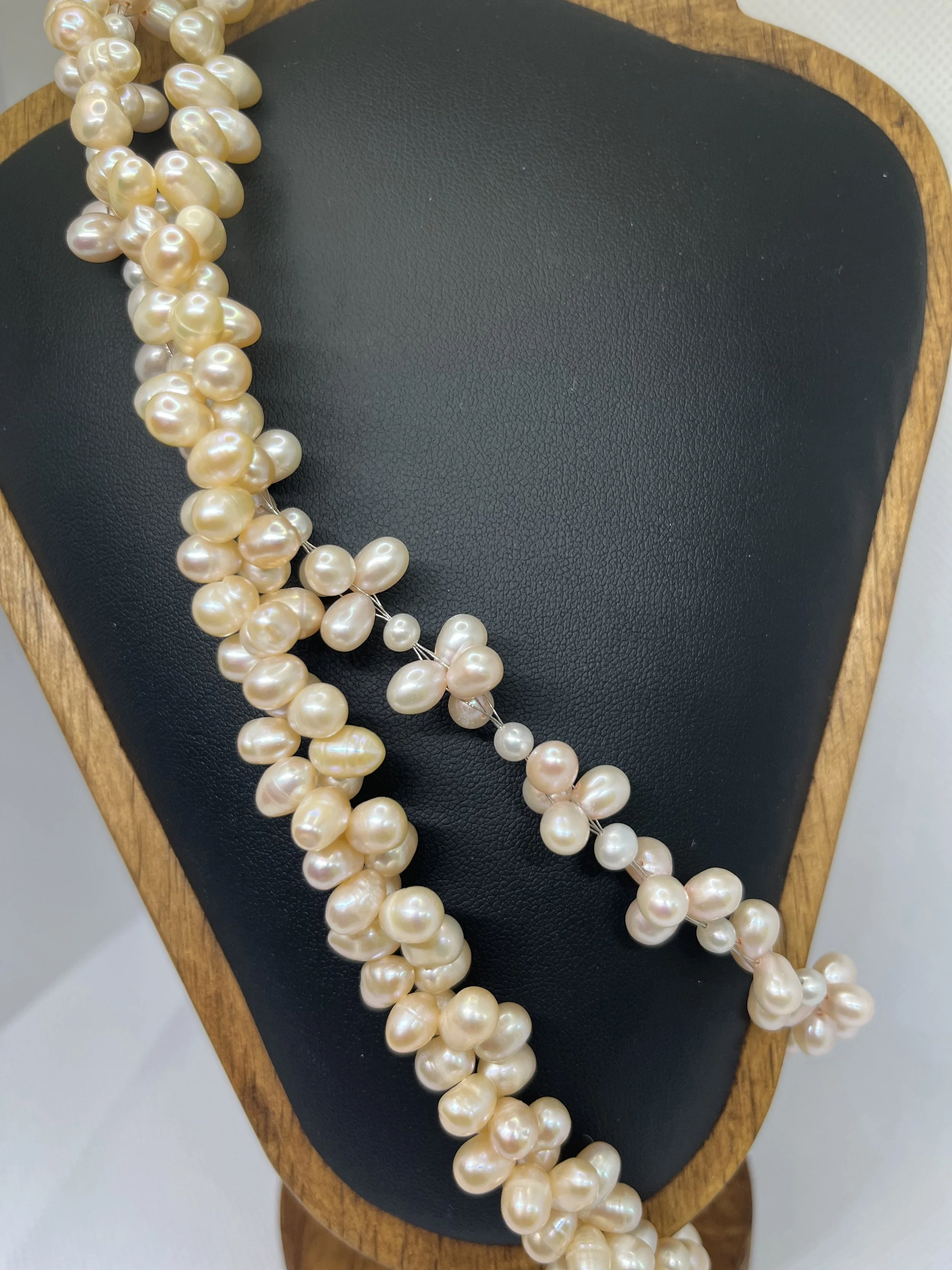 A strand of cream-colored pearls resting on a black leather pad on a wooden jewelry stand.