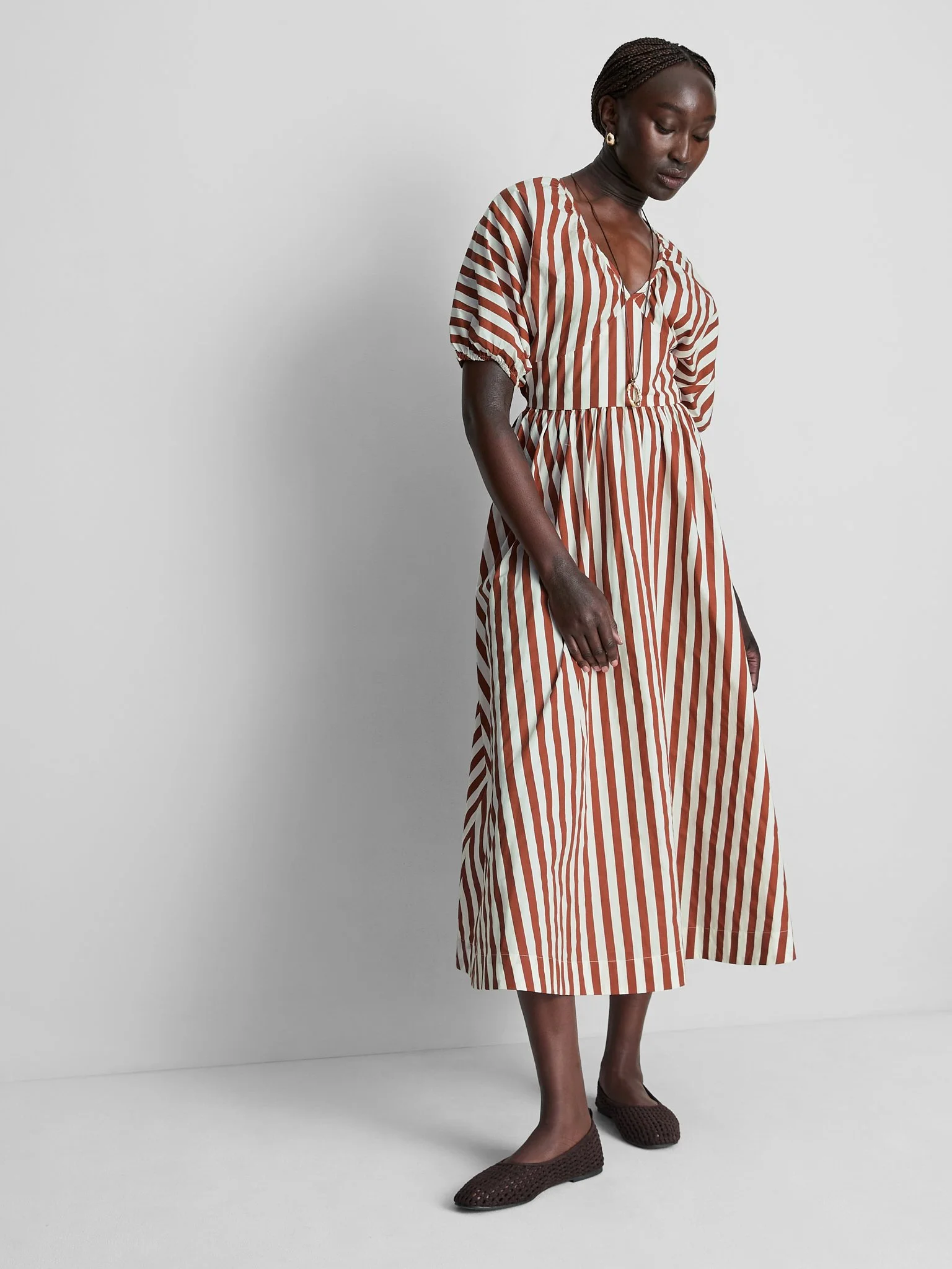 Woman wearing a striped dress and brown woven shoes standing against a plain white background.