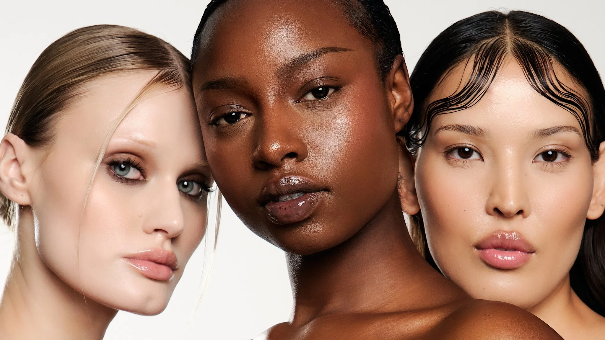Close-up of three diverse women with different skin tones and hair colors, posing closely together.
