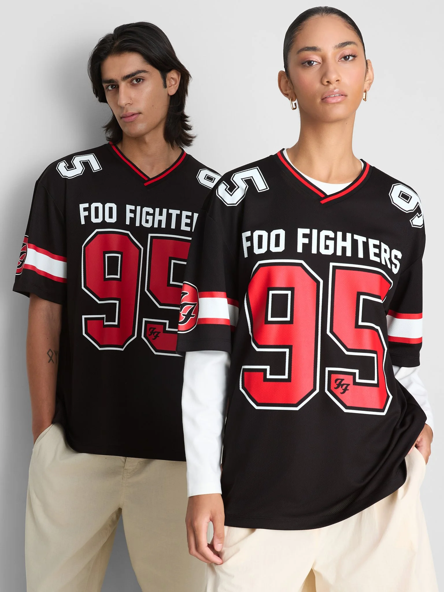 Two models wearing black Foo Fighters hockey jerseys with red and white accents, beige pants, and posing against a plain background.