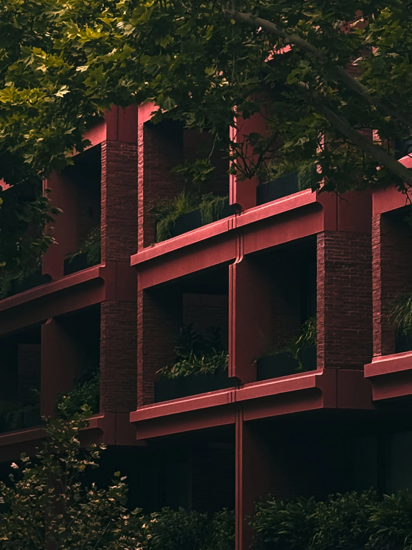 A building with brick walls and balconies, surrounded by green trees and foliage.