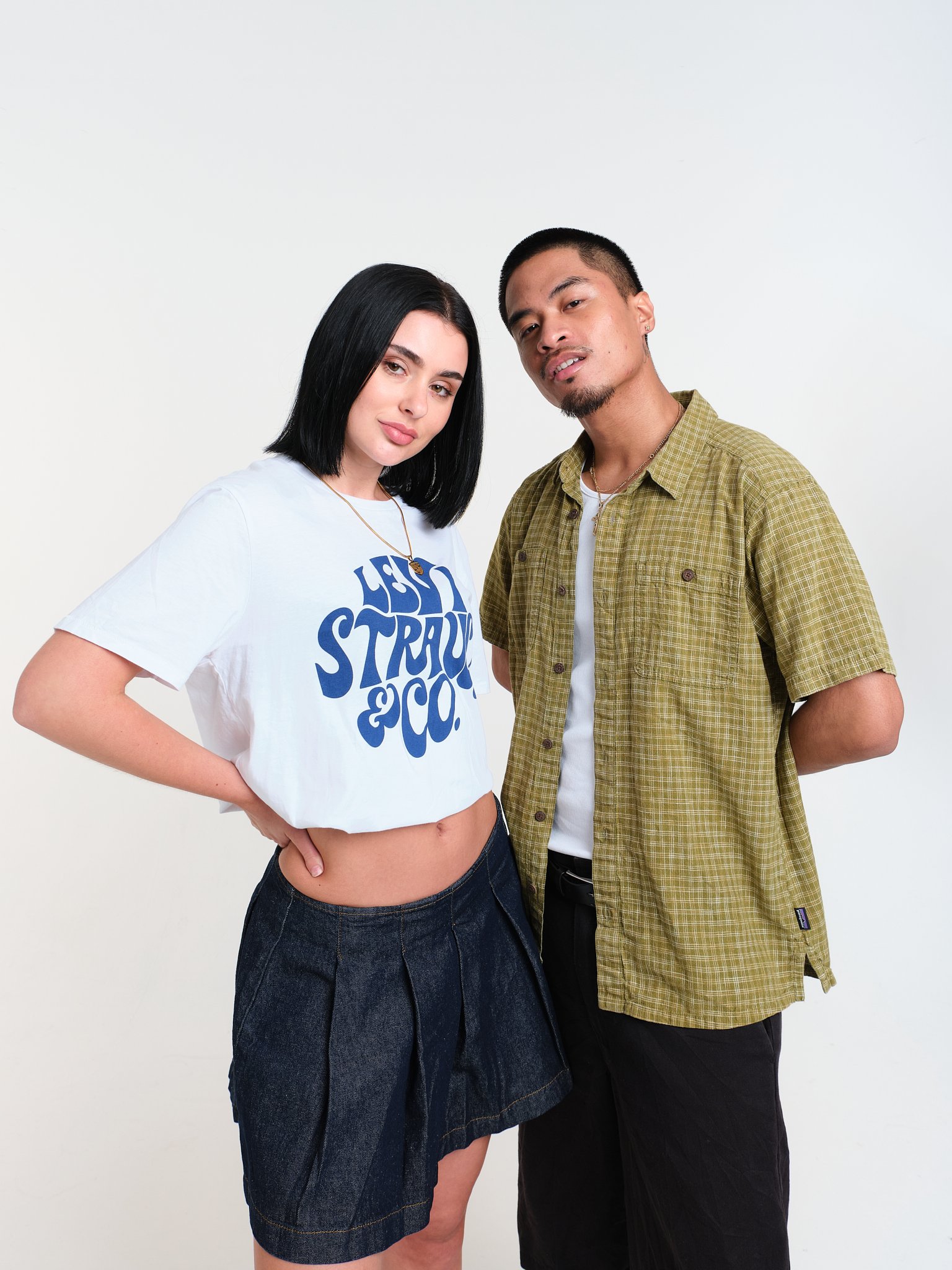A casual portrait of a woman and a man standing together in front of a plain white background, dressed in casual clothing, with neutral expressions and relaxed postures.