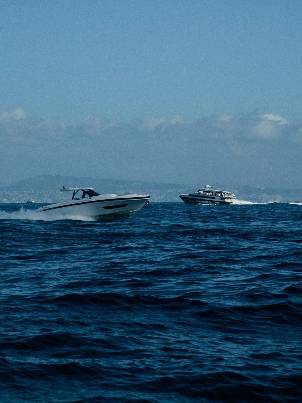 Two boats speeding across the ocean on a clear day with a distant landmass in the background.
