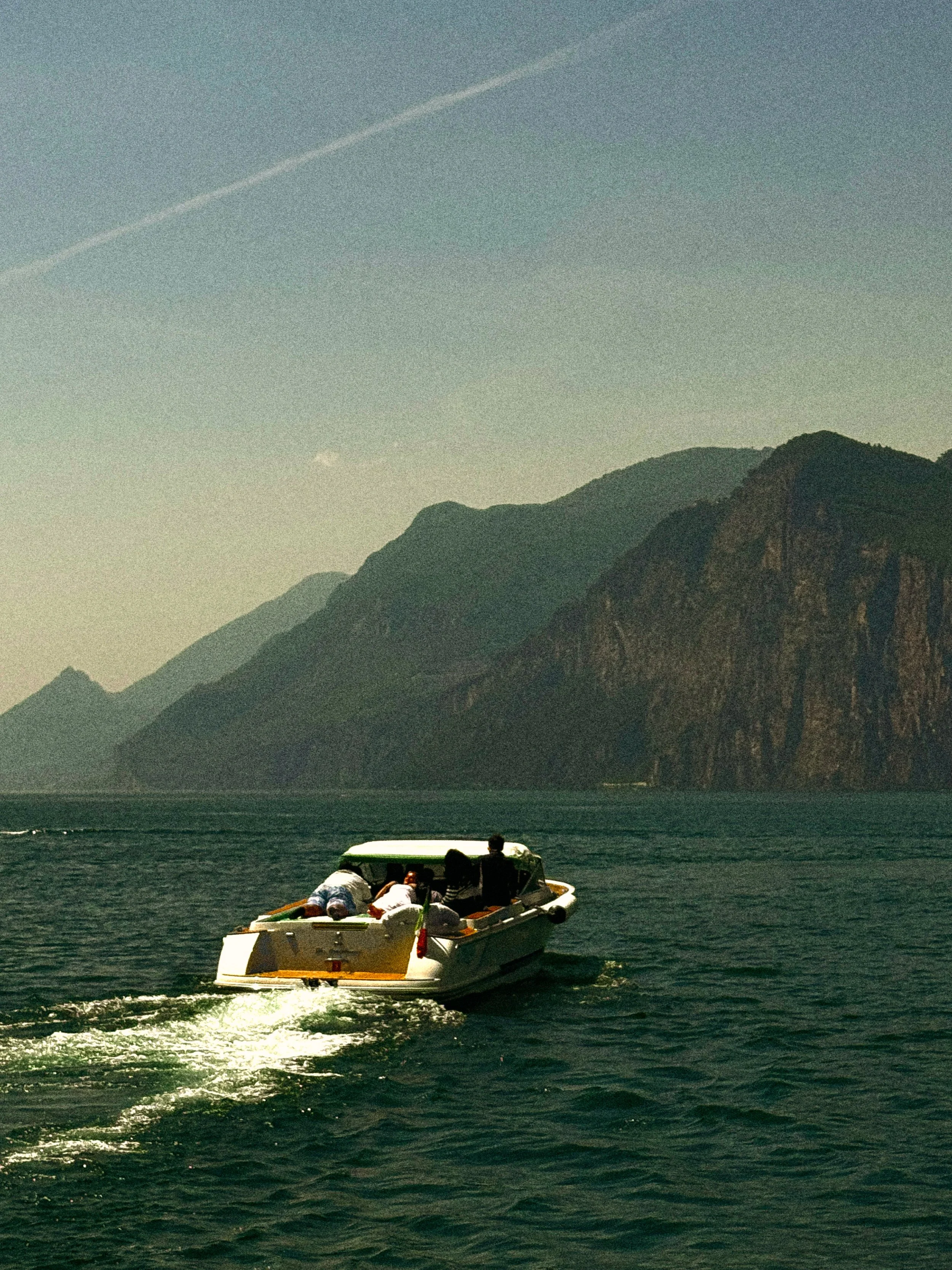 People enjoying a boat ride on a lake or sea, with a backdrop of tall mountain cliffs during the daytime.