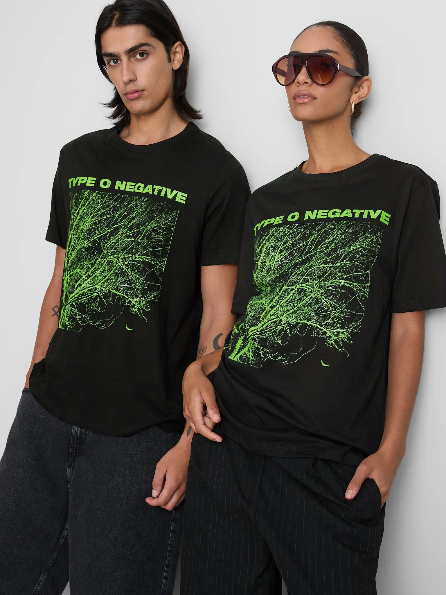 Two models wearing black T-shirts with green graphic designs of tree roots and the words 'Type O Negative' printed on them, standing against a plain white background.