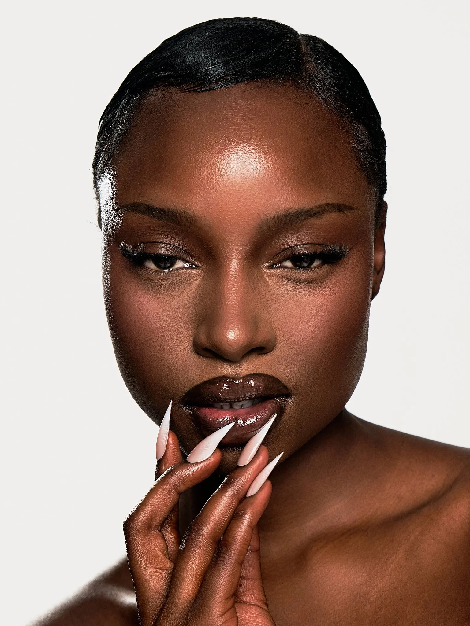 Close-up of a woman with dark skin, short black hair, and long manicured nails. She is touching her lips with her fingers.