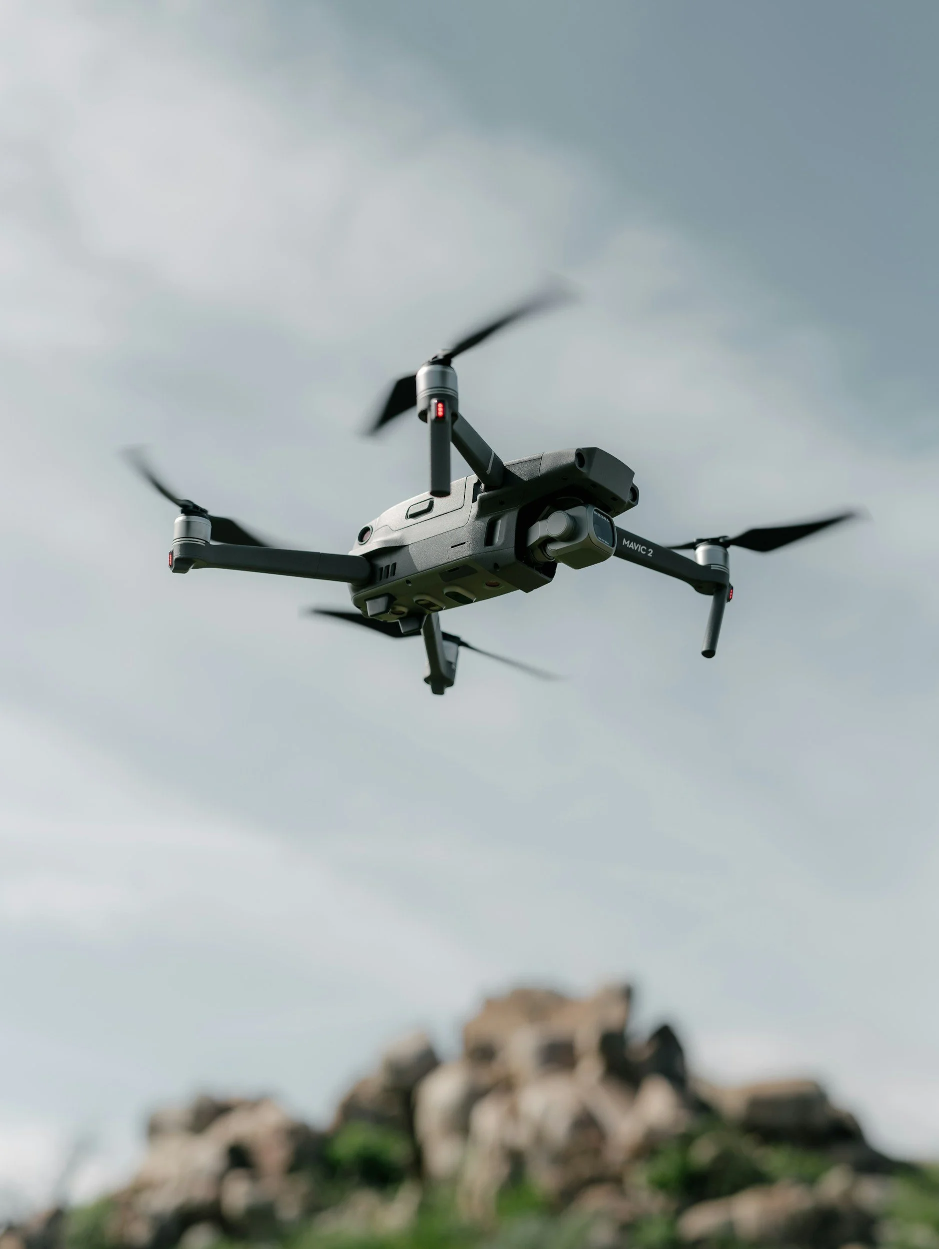 A drone flying in the sky with clouds, with a blurred pile of debris below.