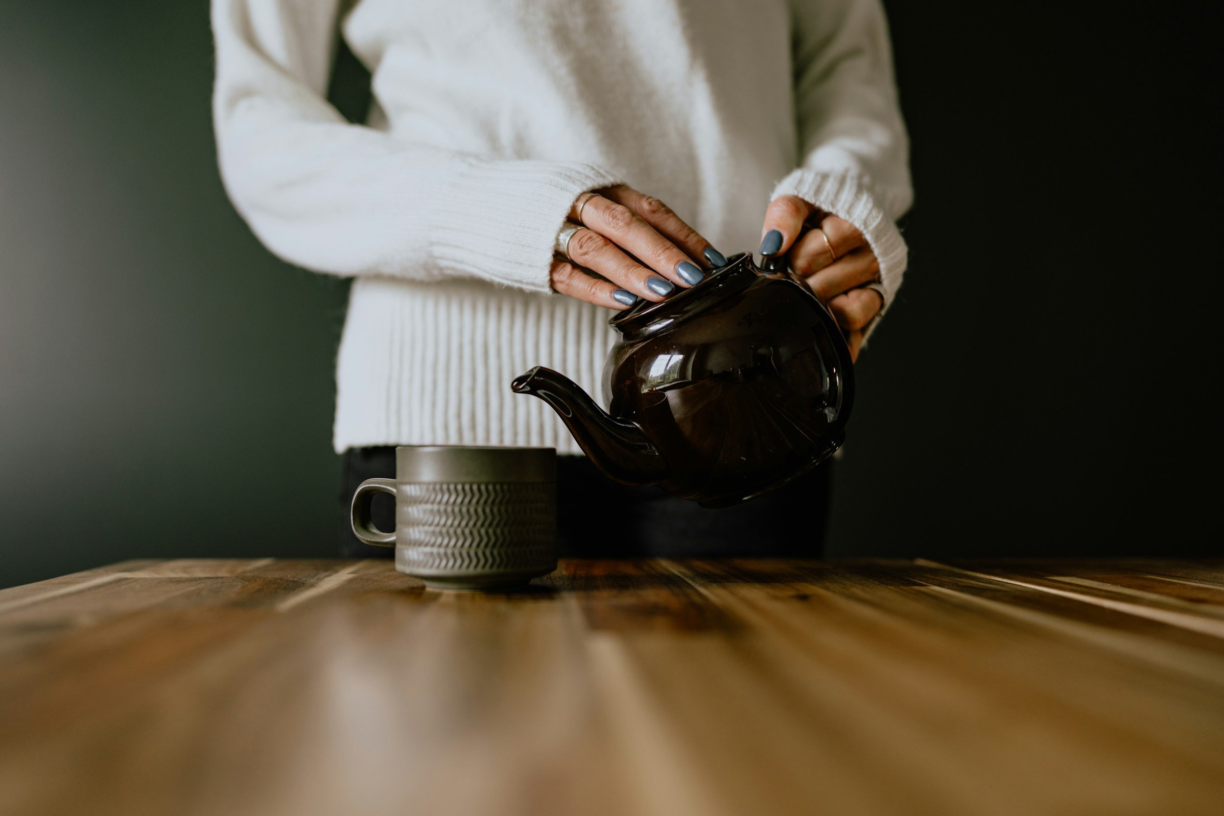 Hands pouring tea from a dark teapot into a cup on a wooden tablePlaceholder