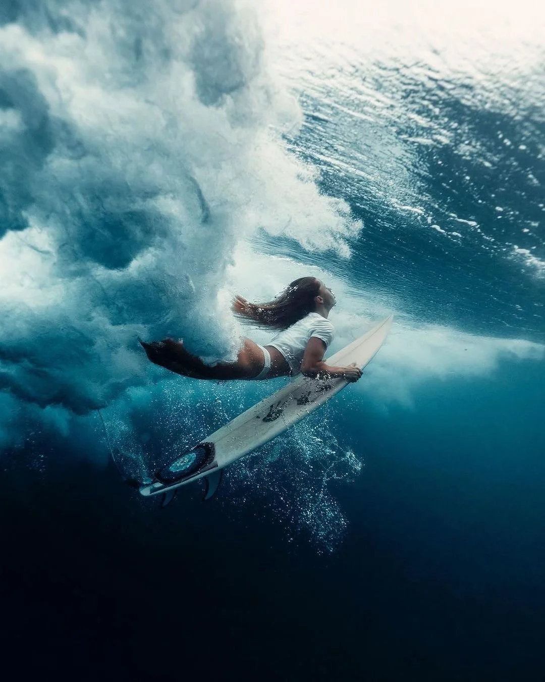 Bumi showcase a woman gracefully surfing on crystal-clear waves in Flores, Indonesia, with a backdrop of stunning clear blue waters.