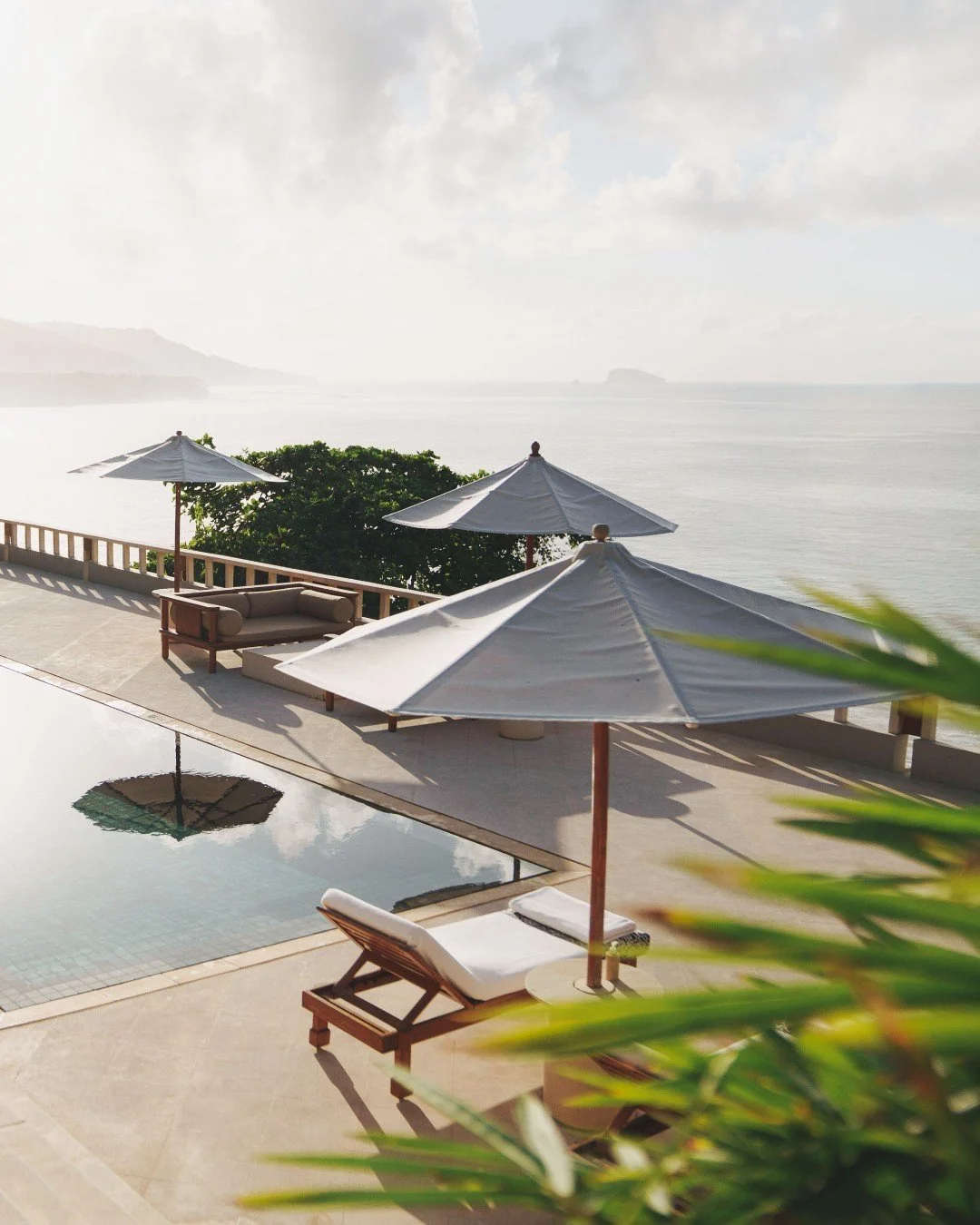 Bumi showcase a stunning view of Amankila resort in Bali, featuring tiered infinity pools overlooking the azure Indian ocean, surrounded by serene timeless luxury.