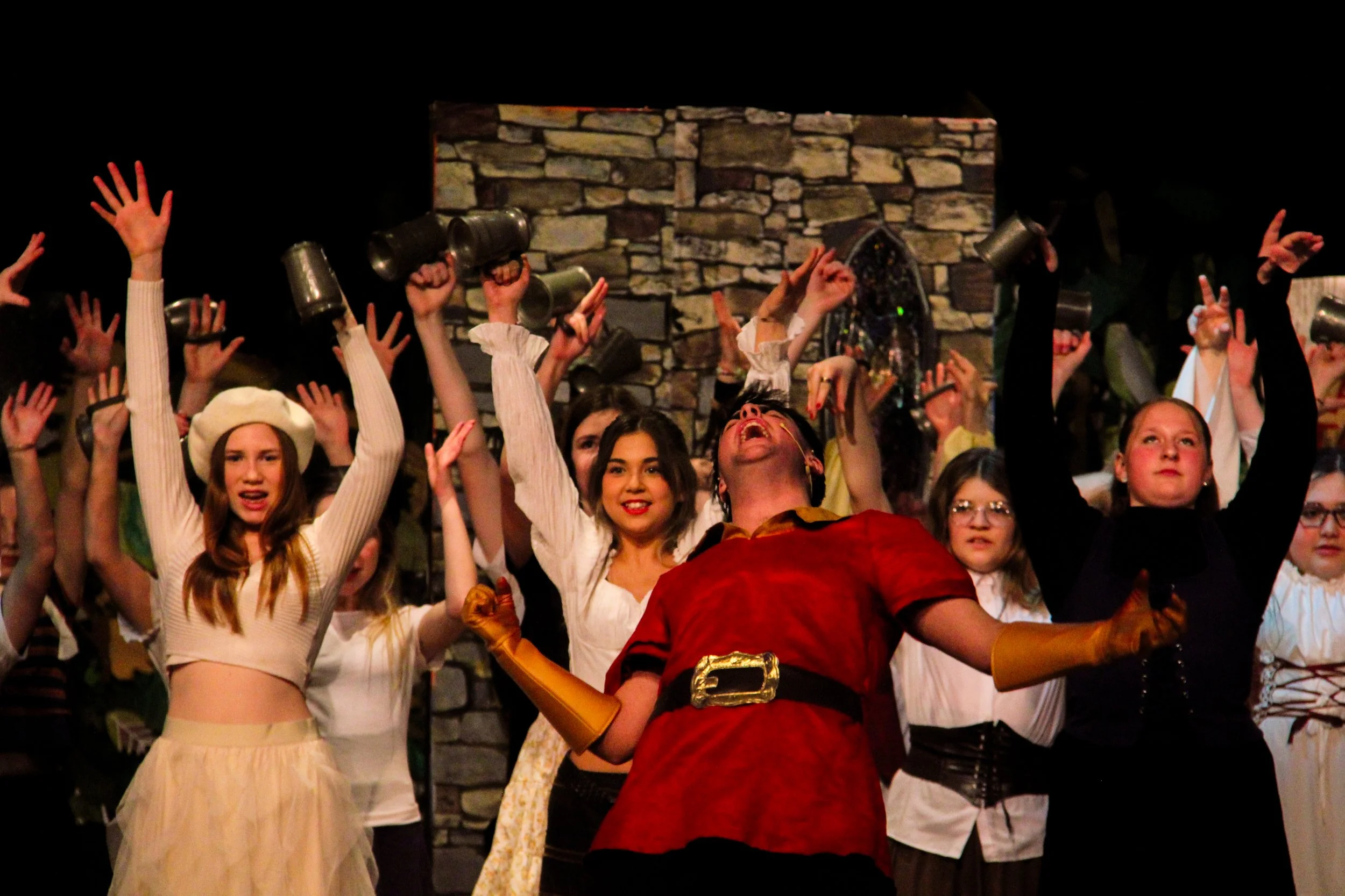 Group of people on stage with arms raised, some holding mugs, and a stone wall background.