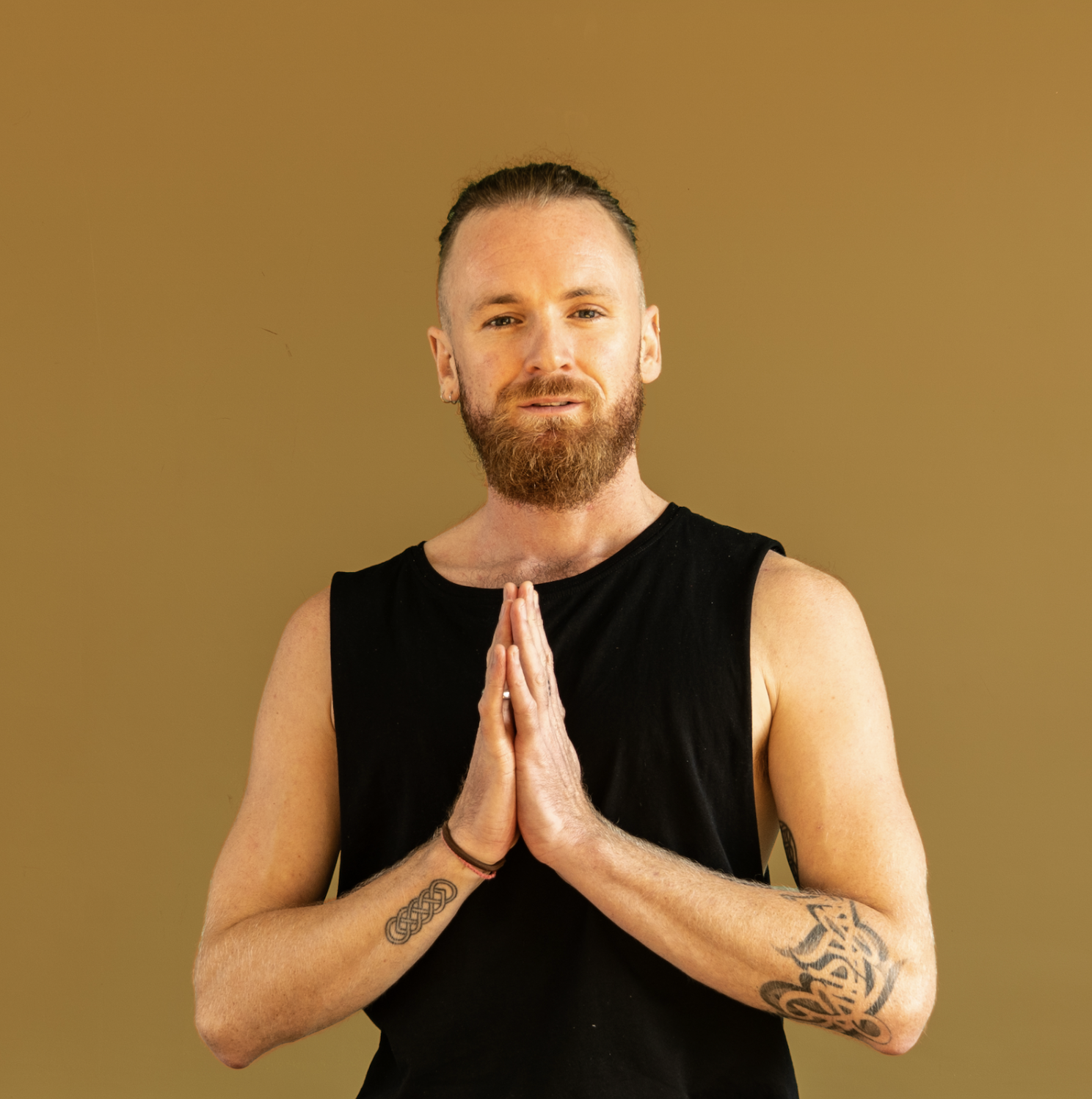 A man with a beard and tattoos on his arms holding his hands together in a prayer position.