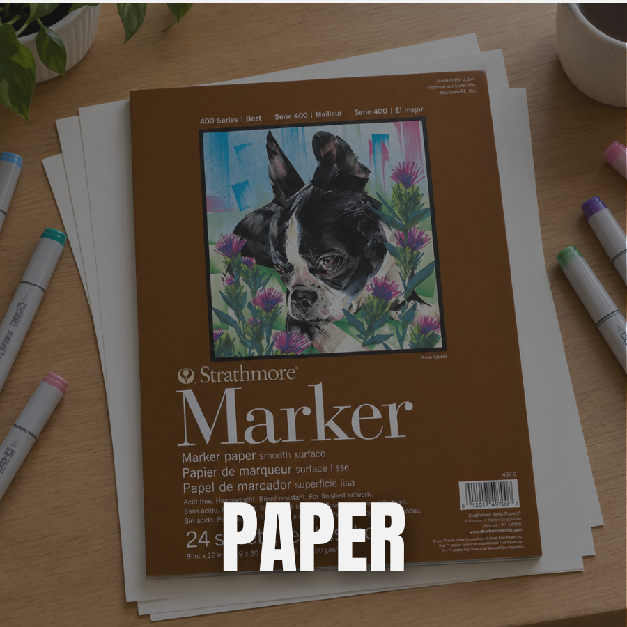 Stacks of paper, colored markers, a plant, and a cup of coffee on a wooden table, with a bonfire-themed art print on top.