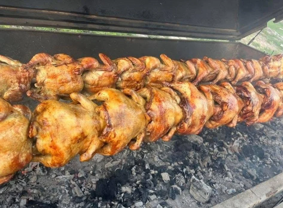 Skewers of whole chickens cooking over charcoal on a grill.