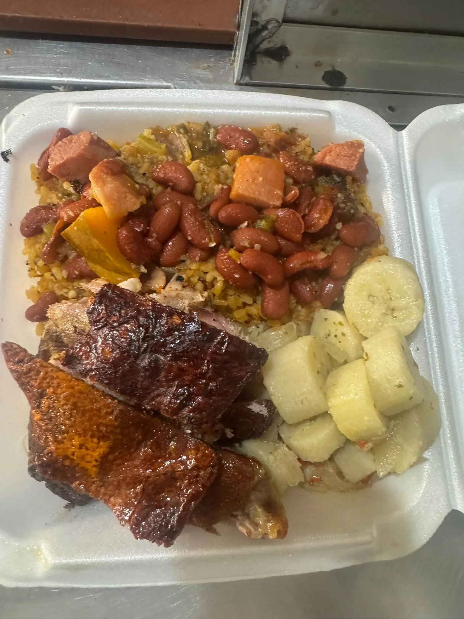 To-go container with baked salmon, baked potatoes, cooked green beans, baked chicken leg, rice, and gravy.