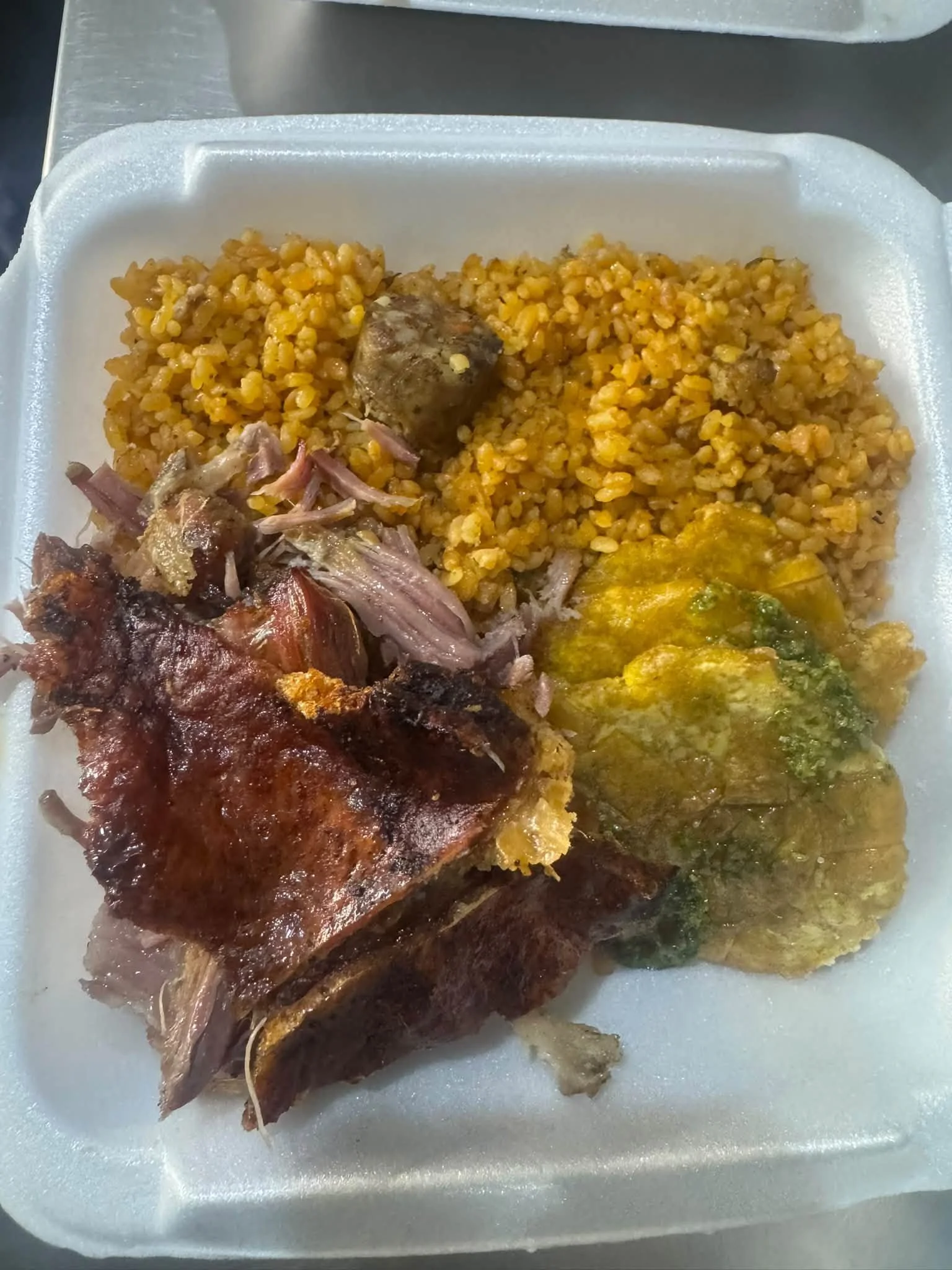 A foam container with rice, a piece of cooked fish, some shredded meat, and collard greens.