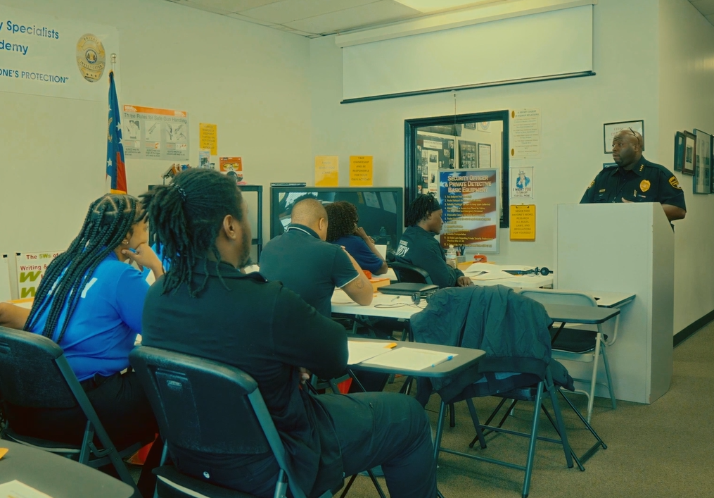 Police officer giving a presentation in a classroom to students seated at desks.