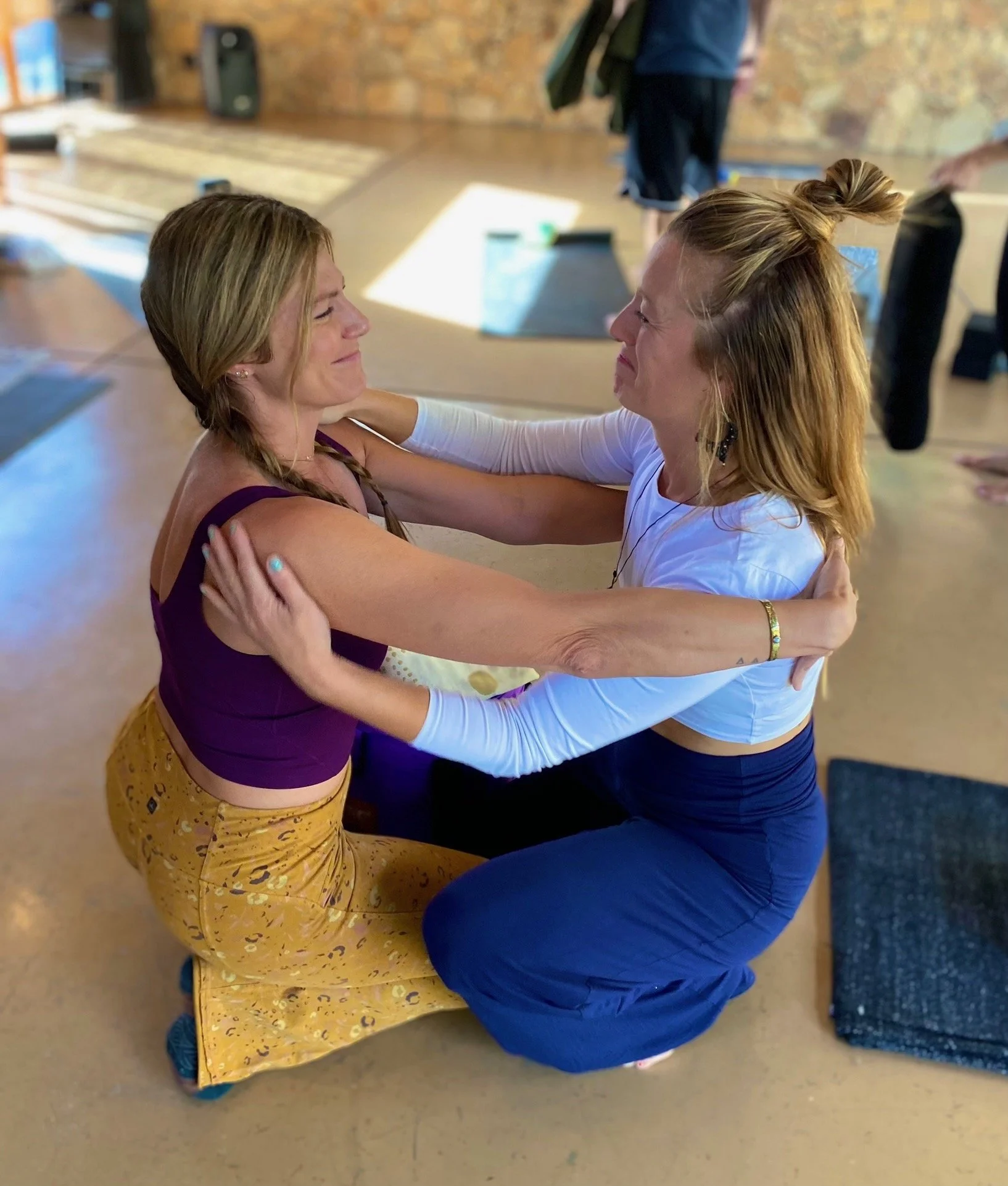 Two women kneeling and embracing indoors during a group activity