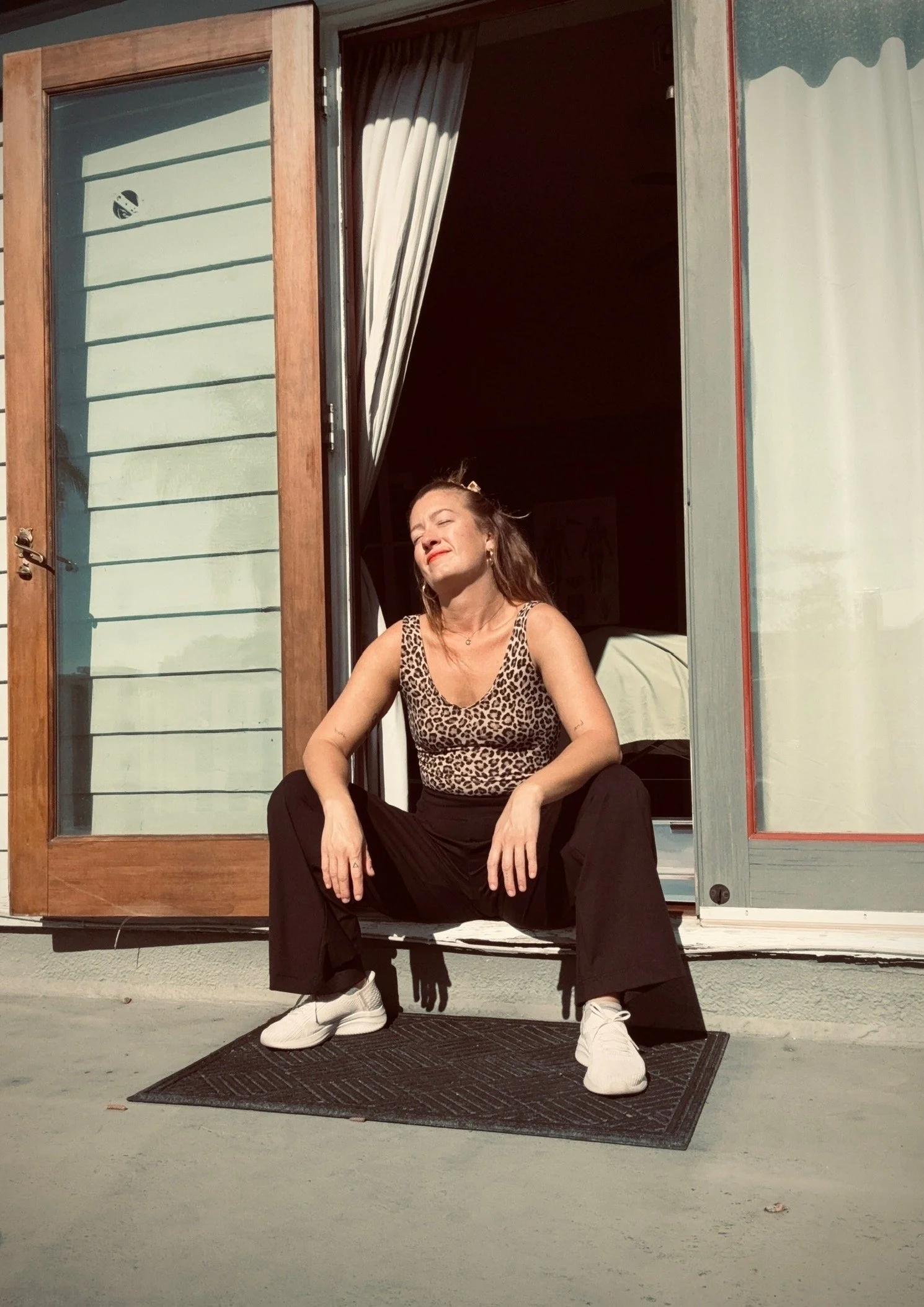 Alyson LeBeau in a leopard-print top and black pants sitting in a sunlit doorway