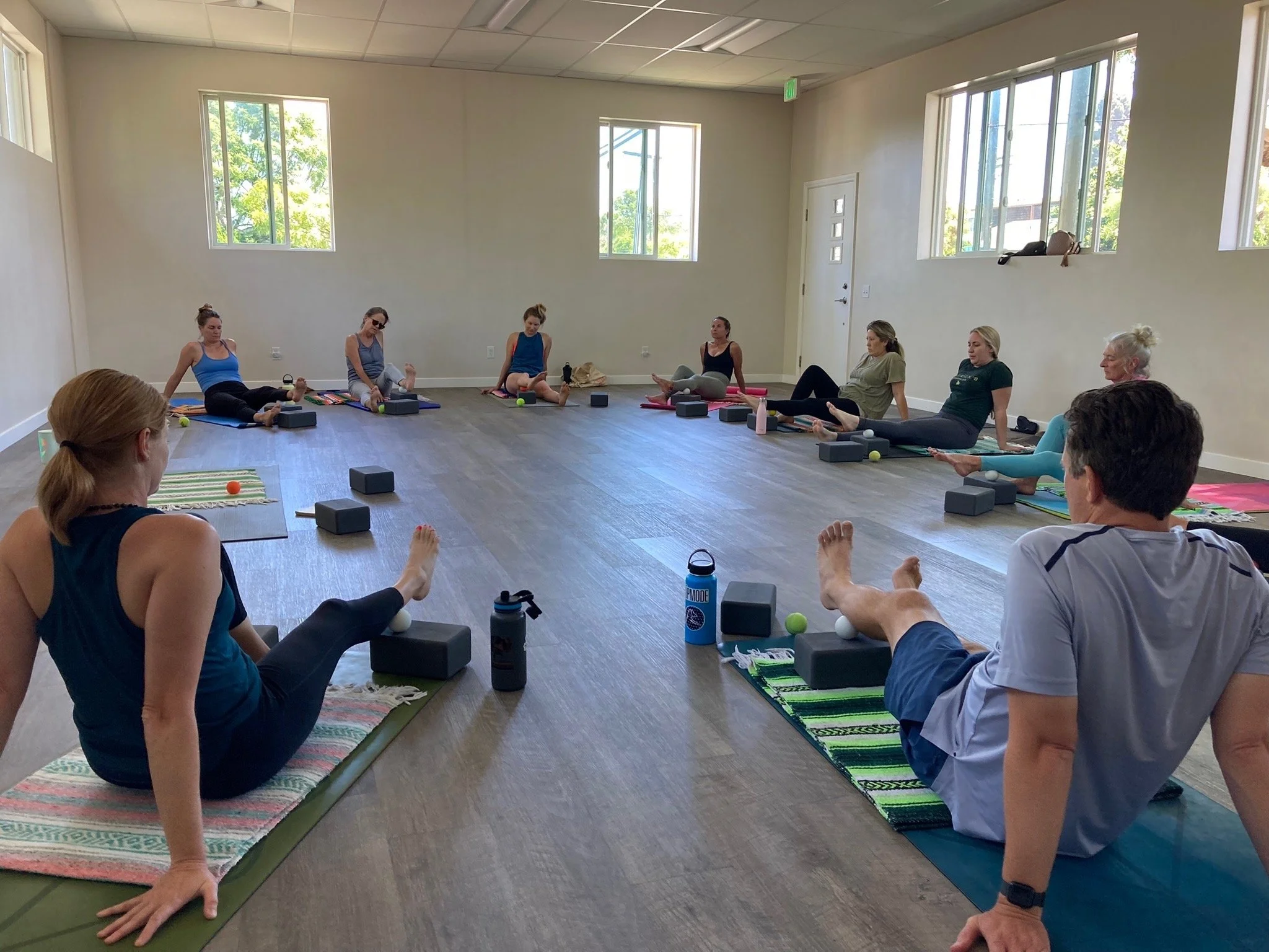 Group yoga class practicing seated poses on mats with yoga blocks in a bright studio