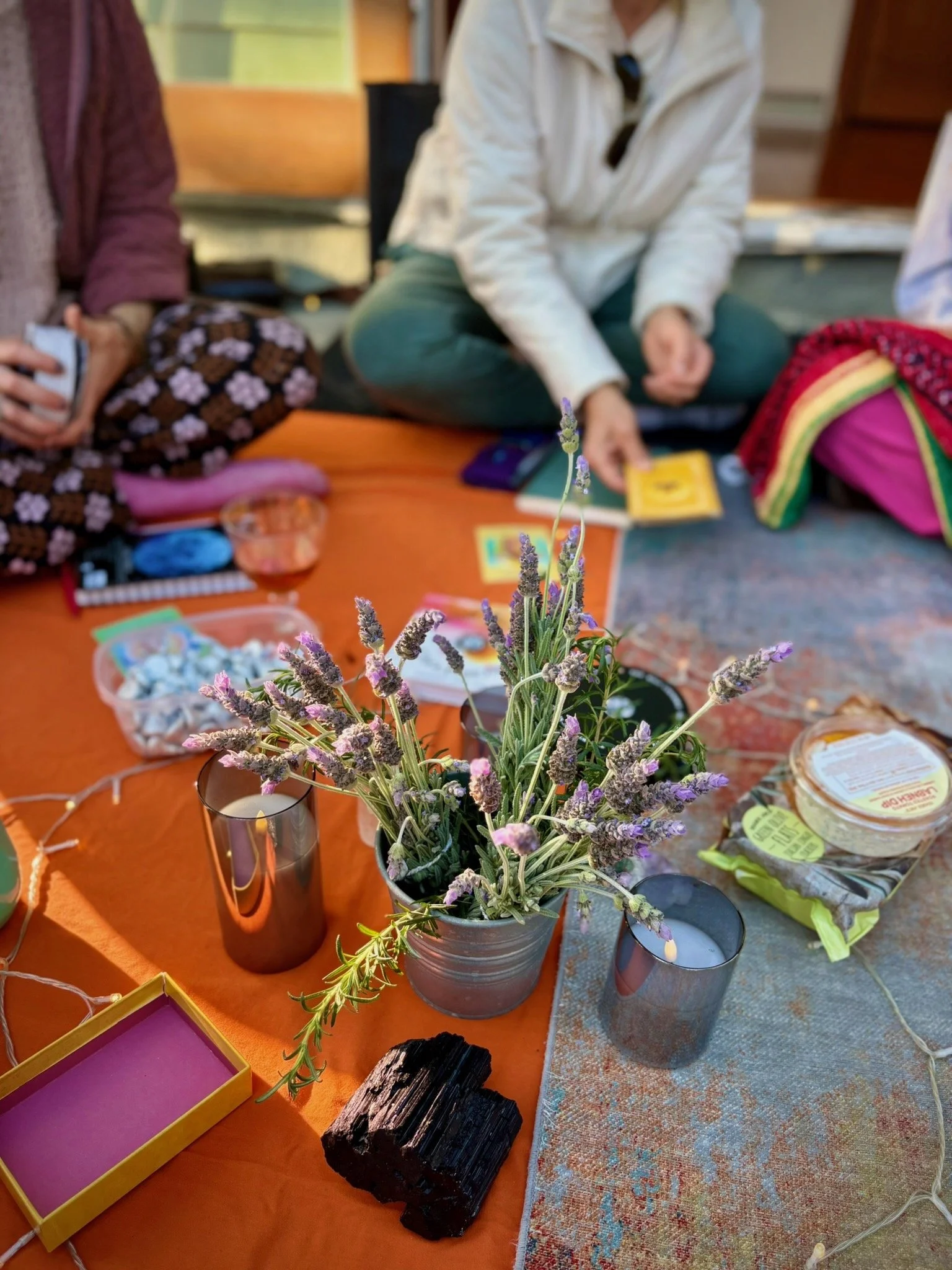 People gathered around a table with lavender flowers, candles, herbs, crystals, and wellness products
