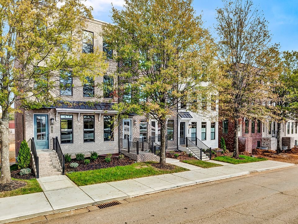 Row of modern townhouses with small front yards and trees lining the sidewalk, in an urban neighborhood.
