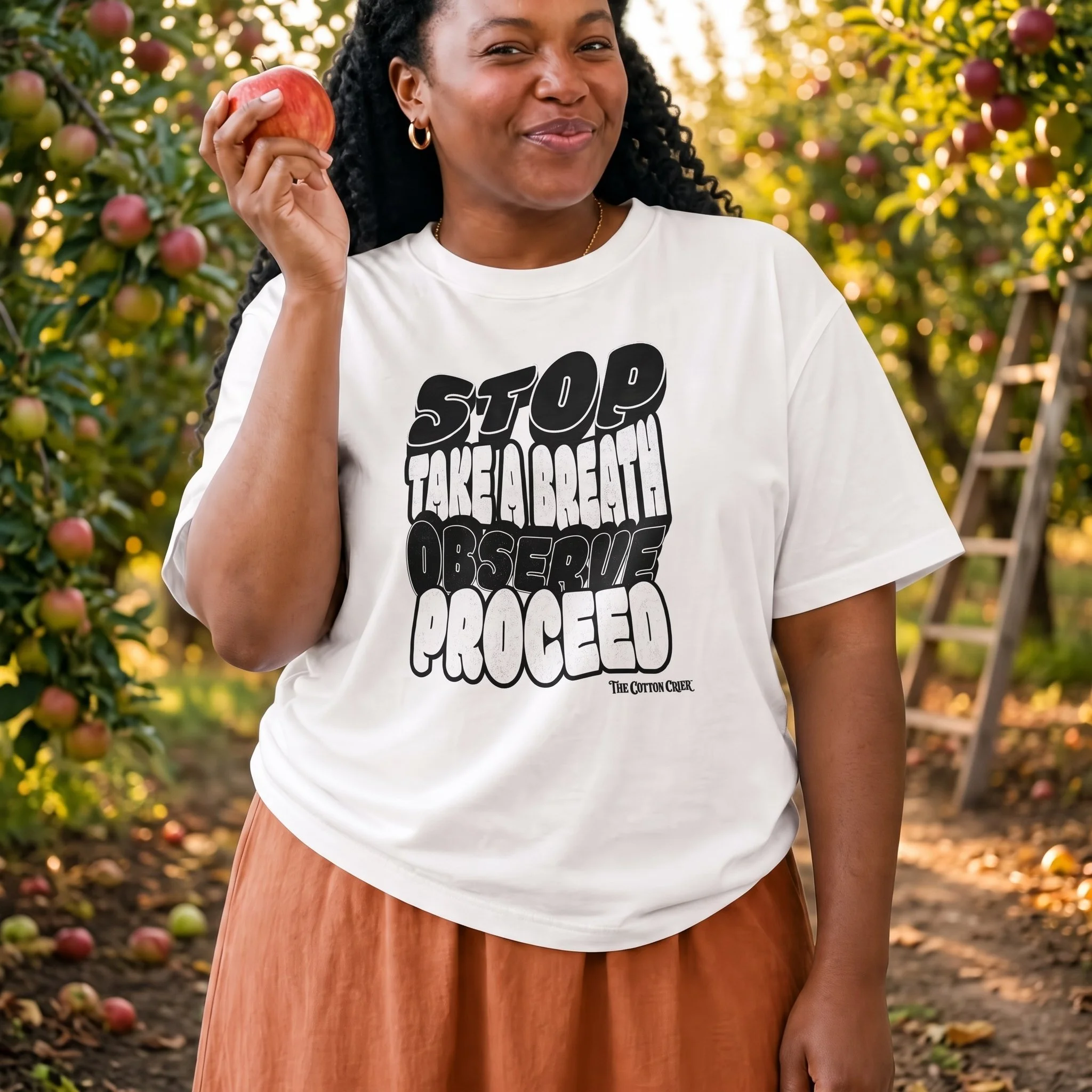 A woman of color holding a red apple to her ear wearing a unisex white cotton t-shirt with the DBT S.T.O.P. skill mind stacks graphics on it by The Cotton Crier.