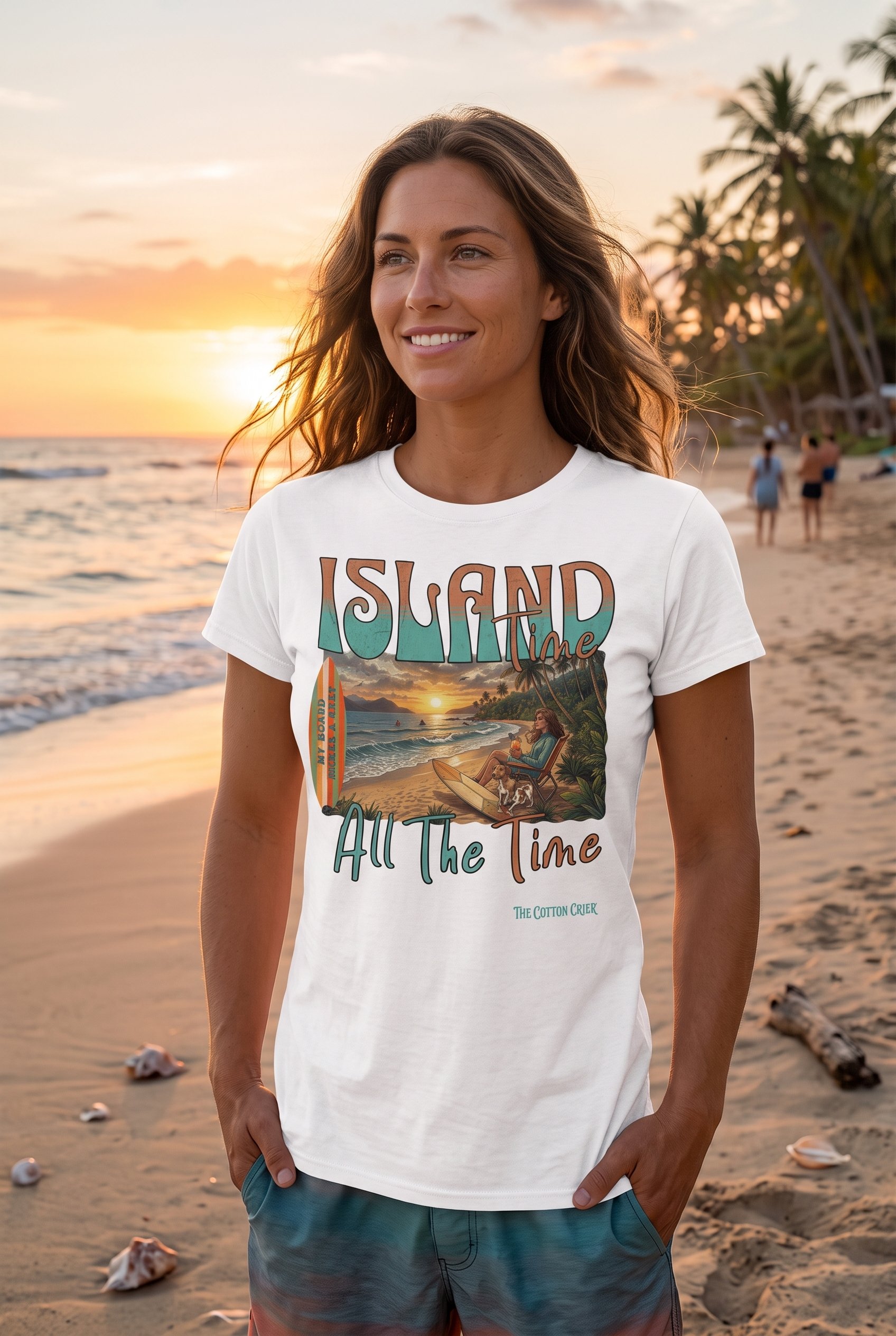 A woman on the beach at sunset, wearing a white T-shirt that says 'Island Time, All The Time' with a tropical island scene, palm trees, and a woman sitting on the beach in the illustration. She is wearing an original design by The Cotton Crier.