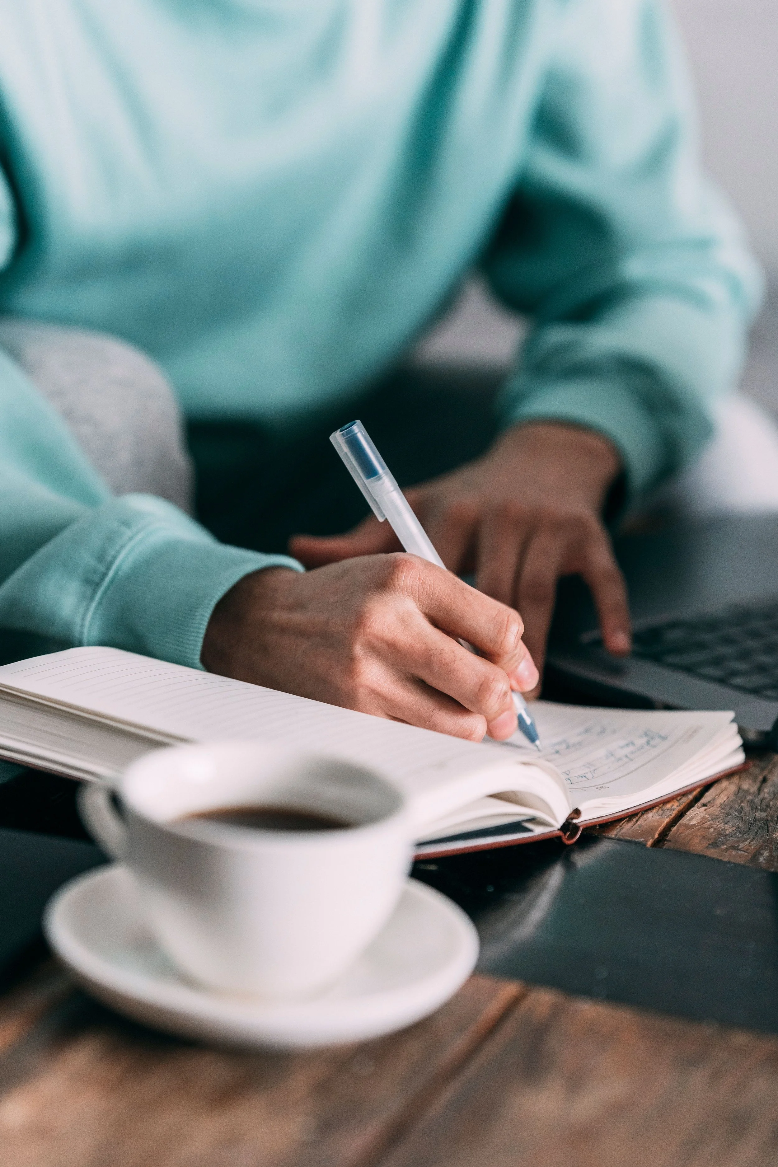 woman with notebook writing on table with laptop