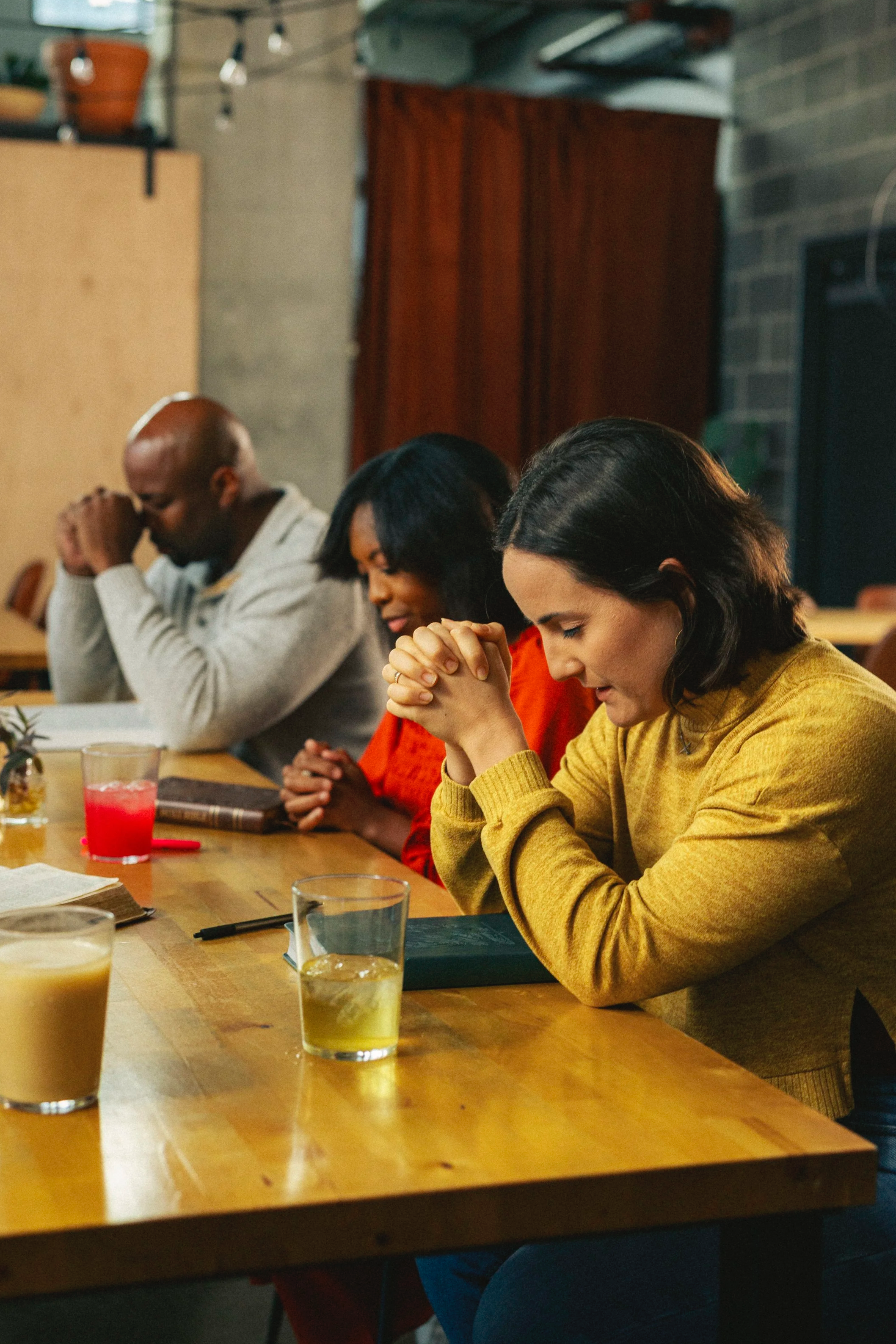 Praying at a table with friends, drinks, and Bibles