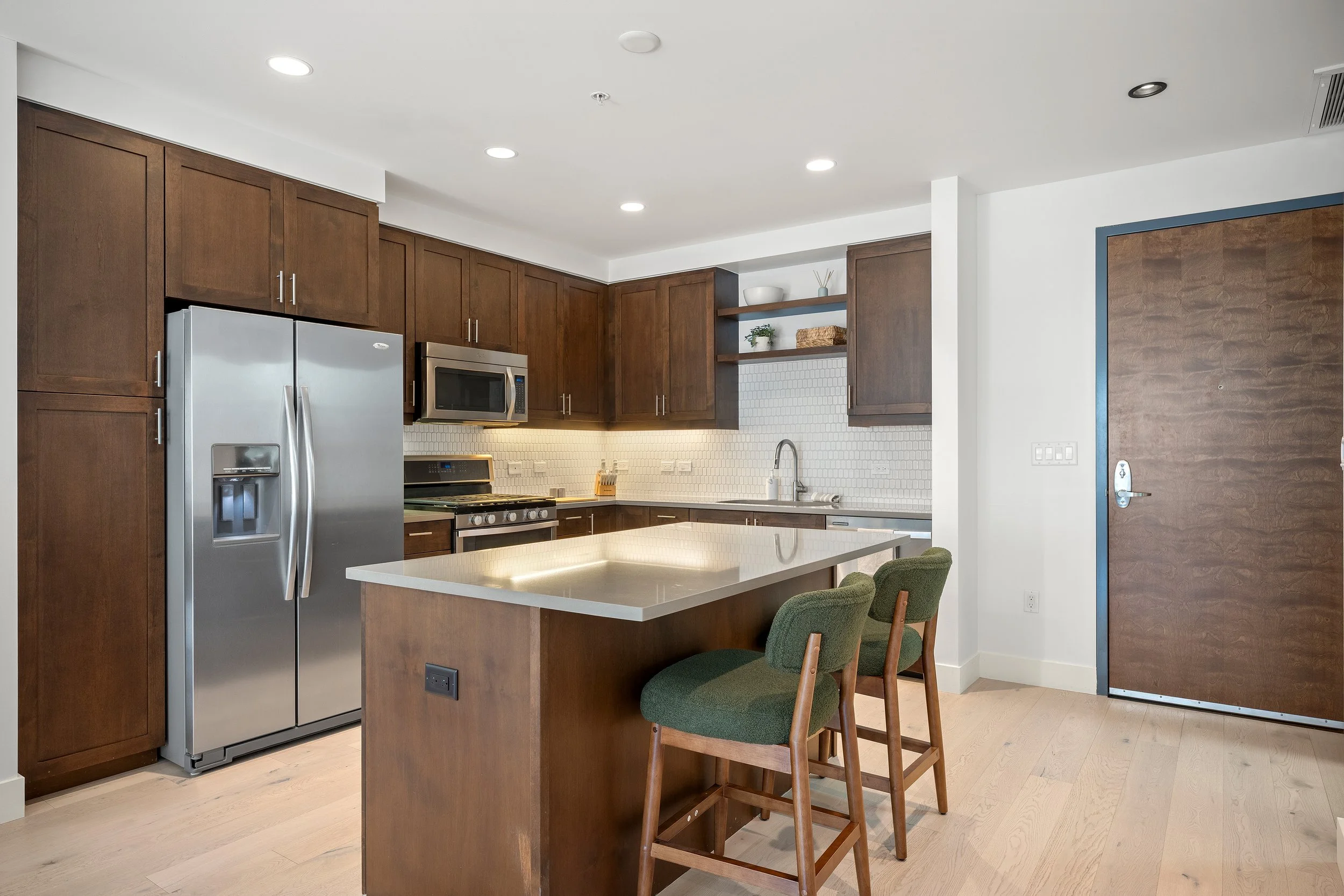 Modern kitchen with dark wood cabinetry, stainless steel appliances, a large island, and bar seating.