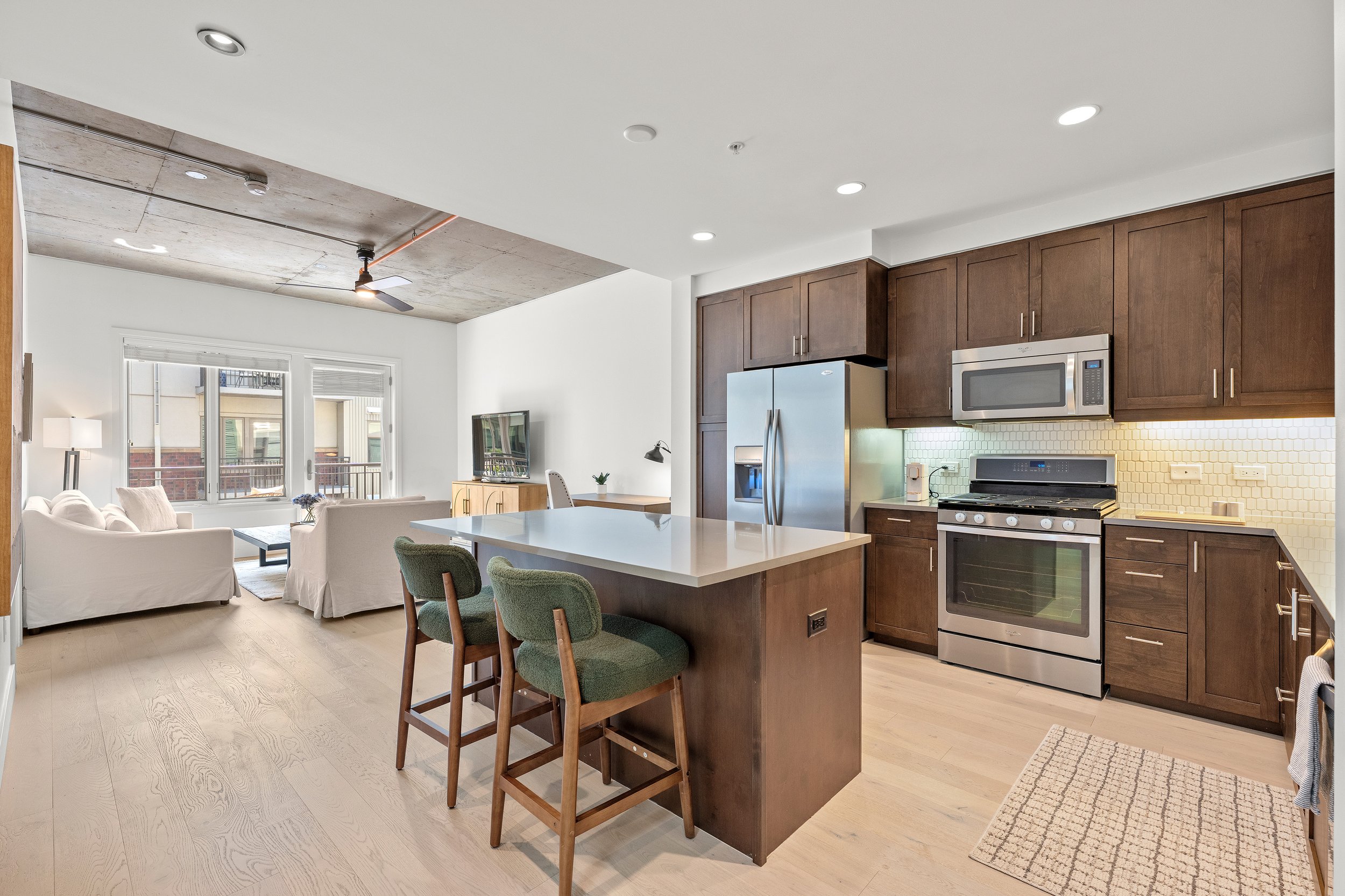 Open kitchen and dining area with a large island, dark wood cabinetry, and bright neutral finishes.