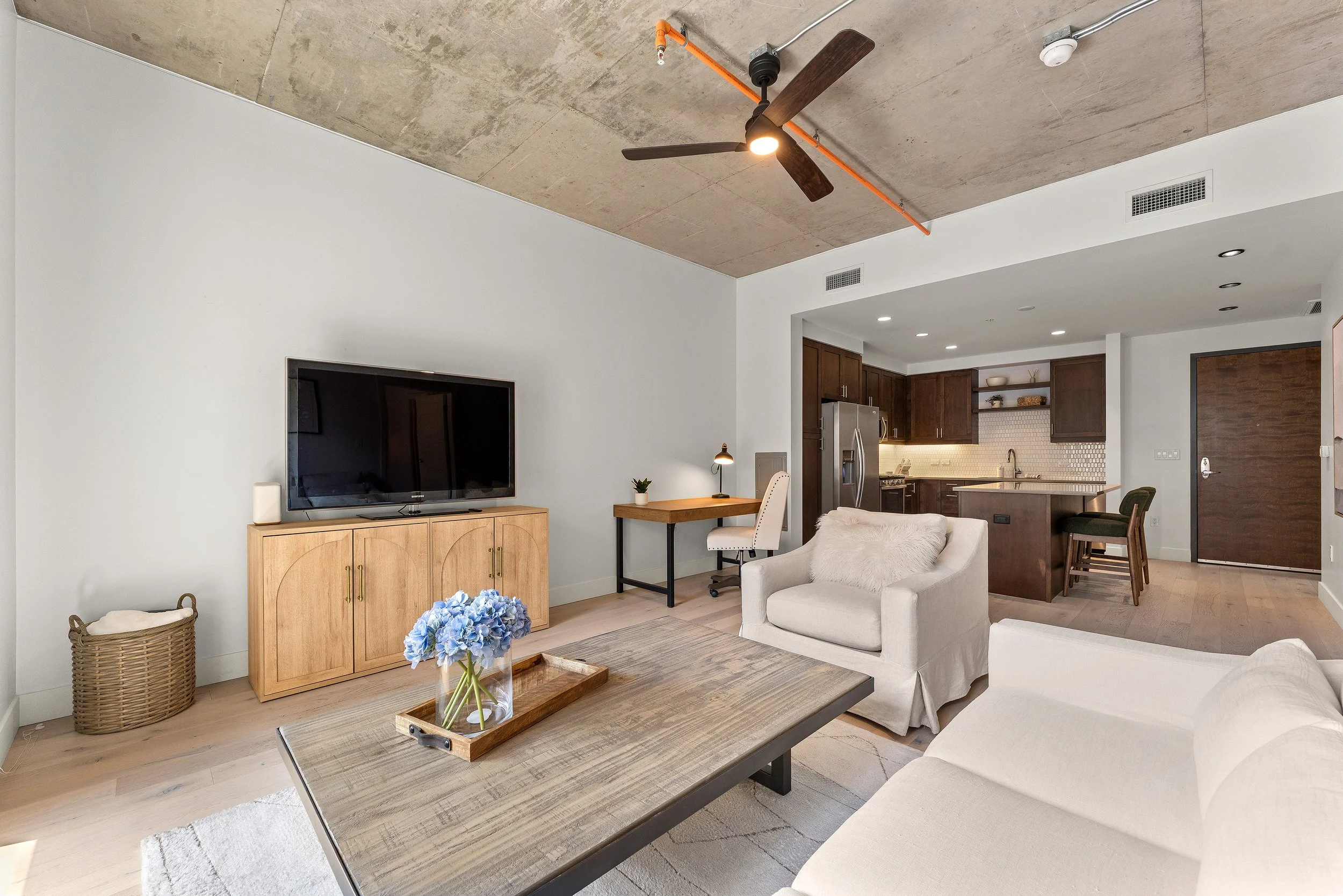 Living room with neutral furnishings, television console, wood flooring, and textured ceiling details.