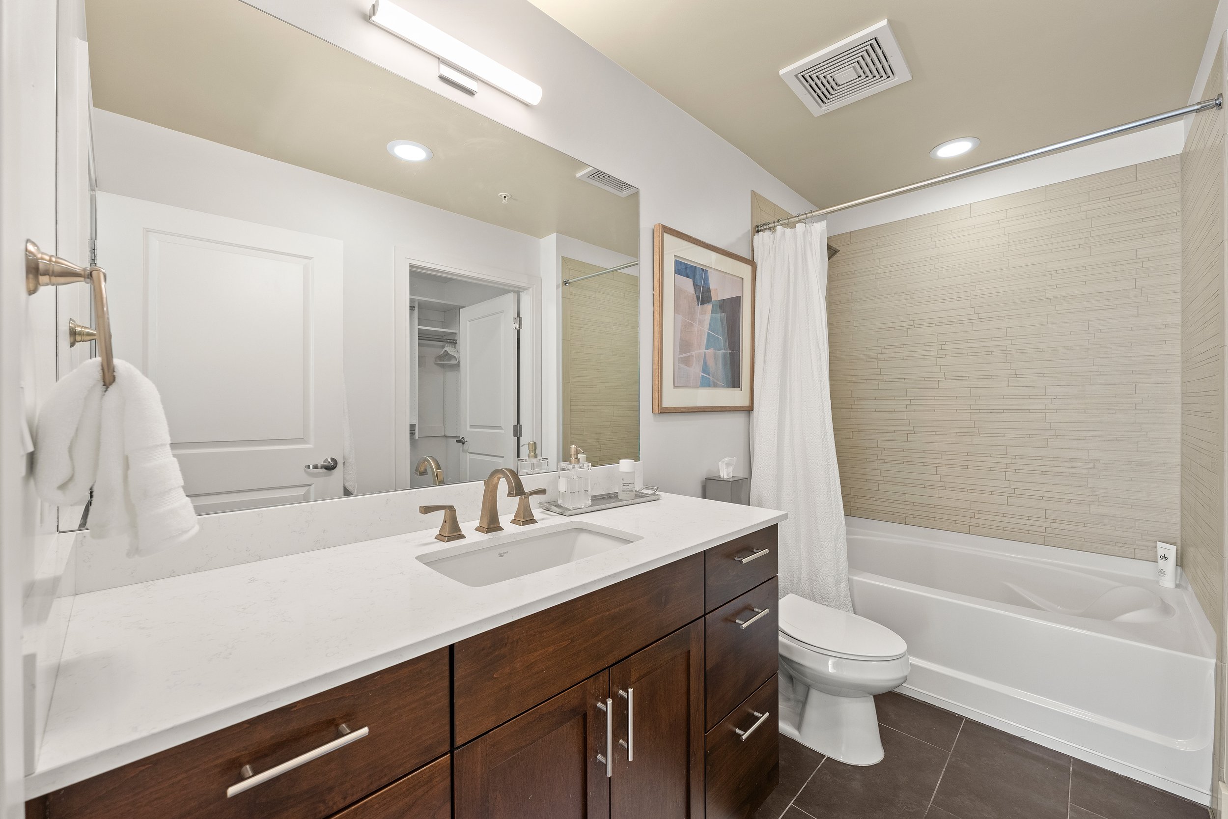 Bathroom with wood vanity, white countertop, large mirror, and tub-shower combination.