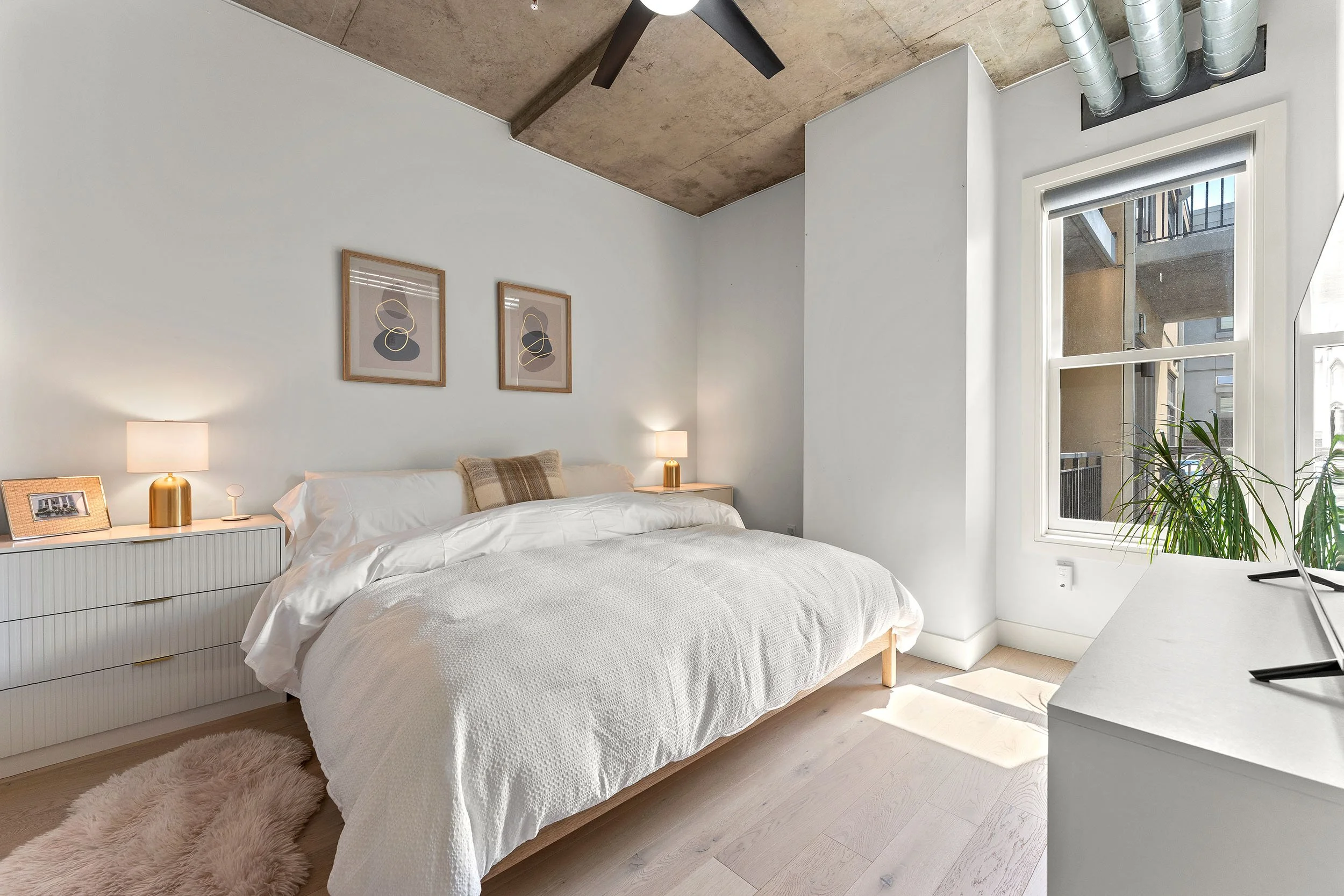 Bedroom with neutral bedding, upholstered headboard, and soft natural light.