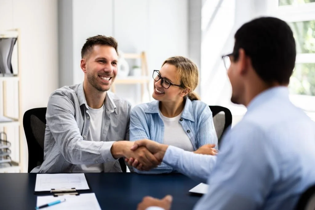 A man and woman smiling and shaking hands with a man in a business setting.