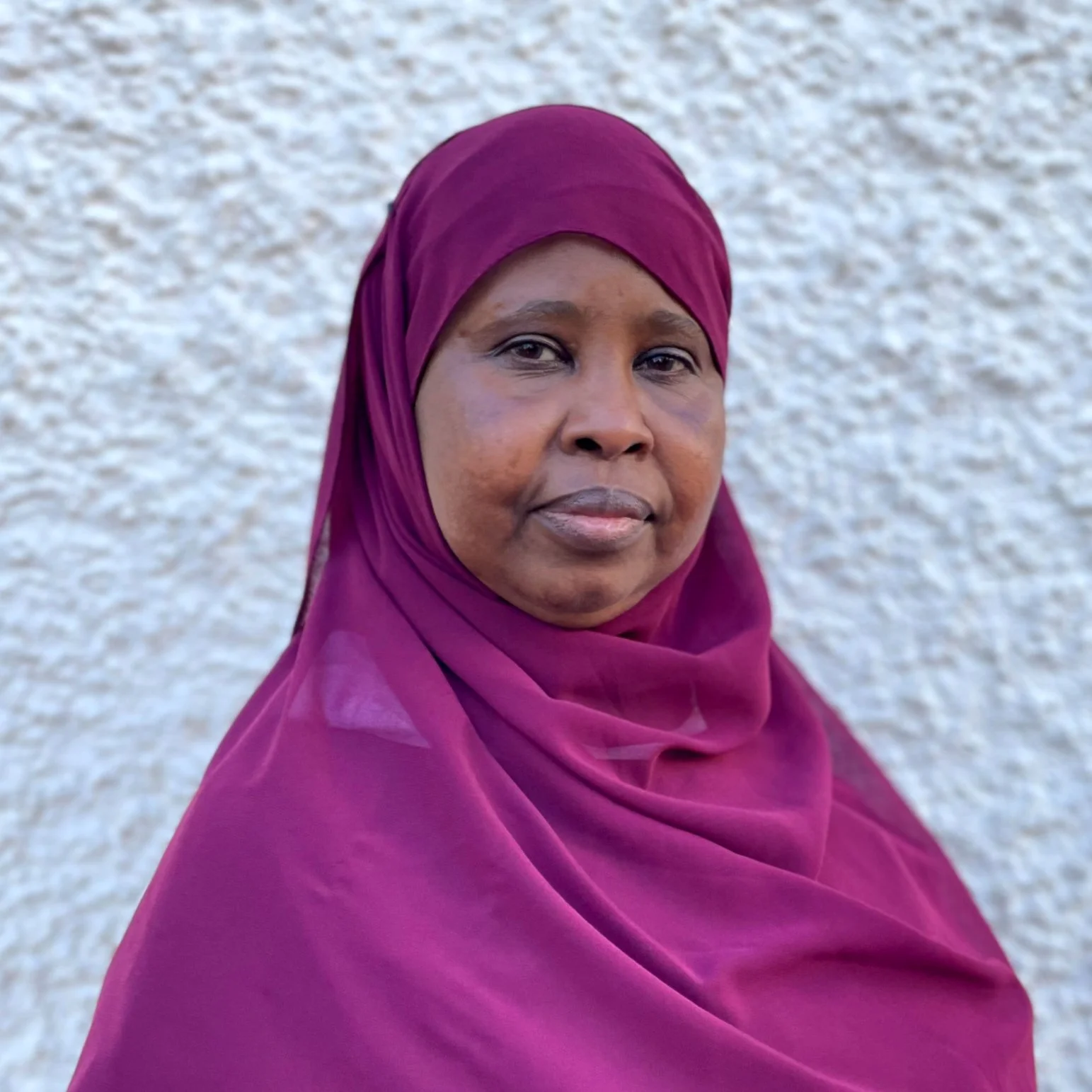 En kvinna i en lila hijab poserar framför en vit vägg.