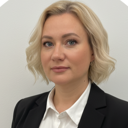En professionell kvinna med blont, lockigt hår, iklädd vit skjorta och svart kavaj, står framför en ljus vägg.