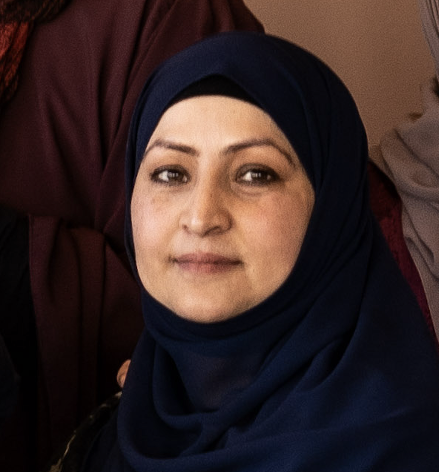 En kvinna med slöja som tittar mot kameran, omgiven av andra personer.