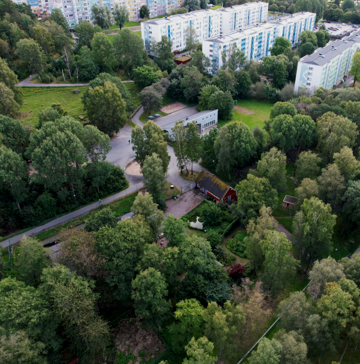 Flygbild av ett grönt område med många träd, vägar och några byggnader i en bostadsområde.