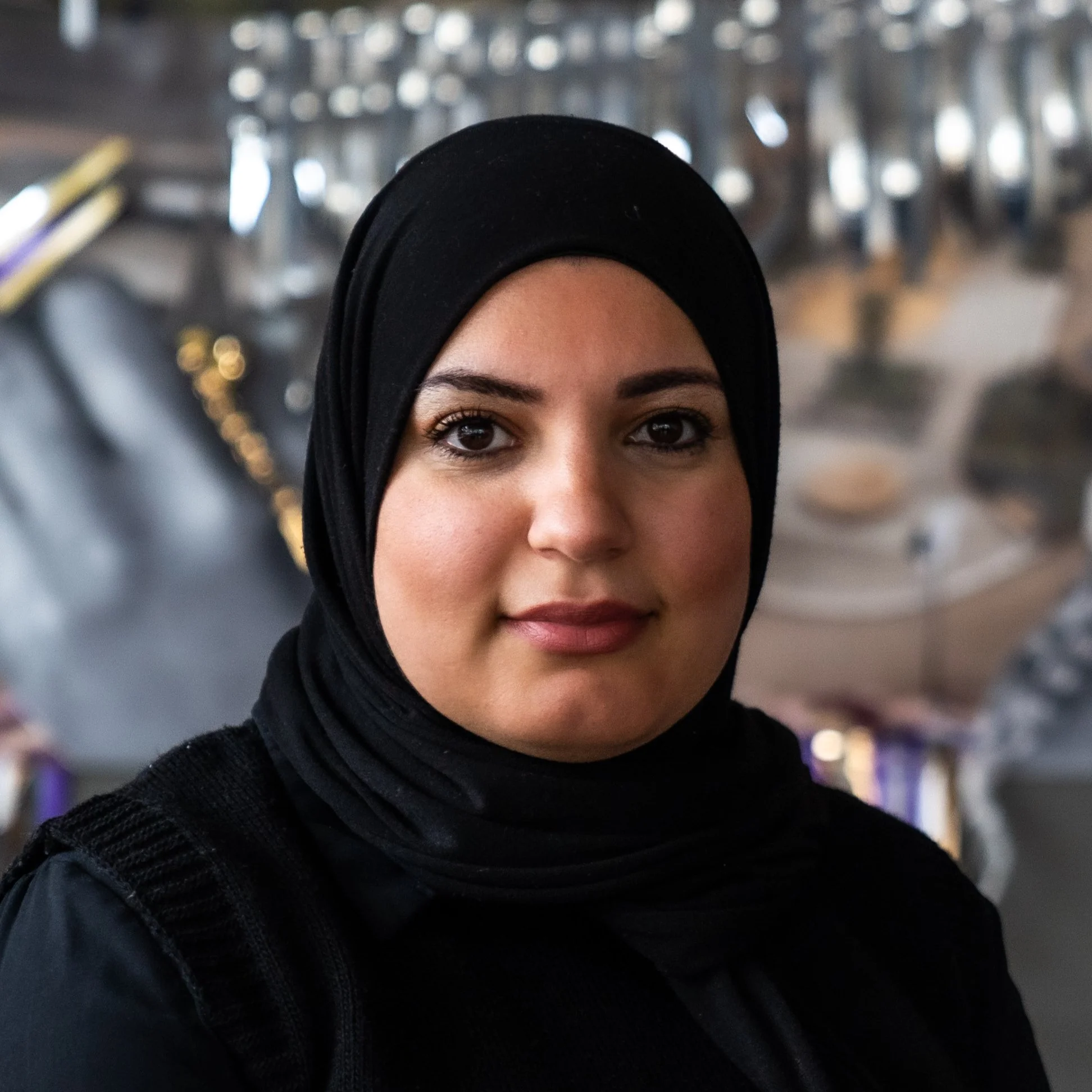 En ung kvinna med mörka ögon och mörk hud och svart hijab, fotograferad i en butik eller ett köpcentrum.