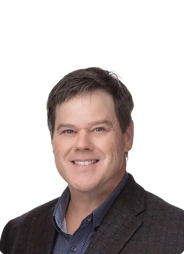 Professional headshot of Dr. Mihills, wearing a dark blazer and blue shirt, against a plain white background.