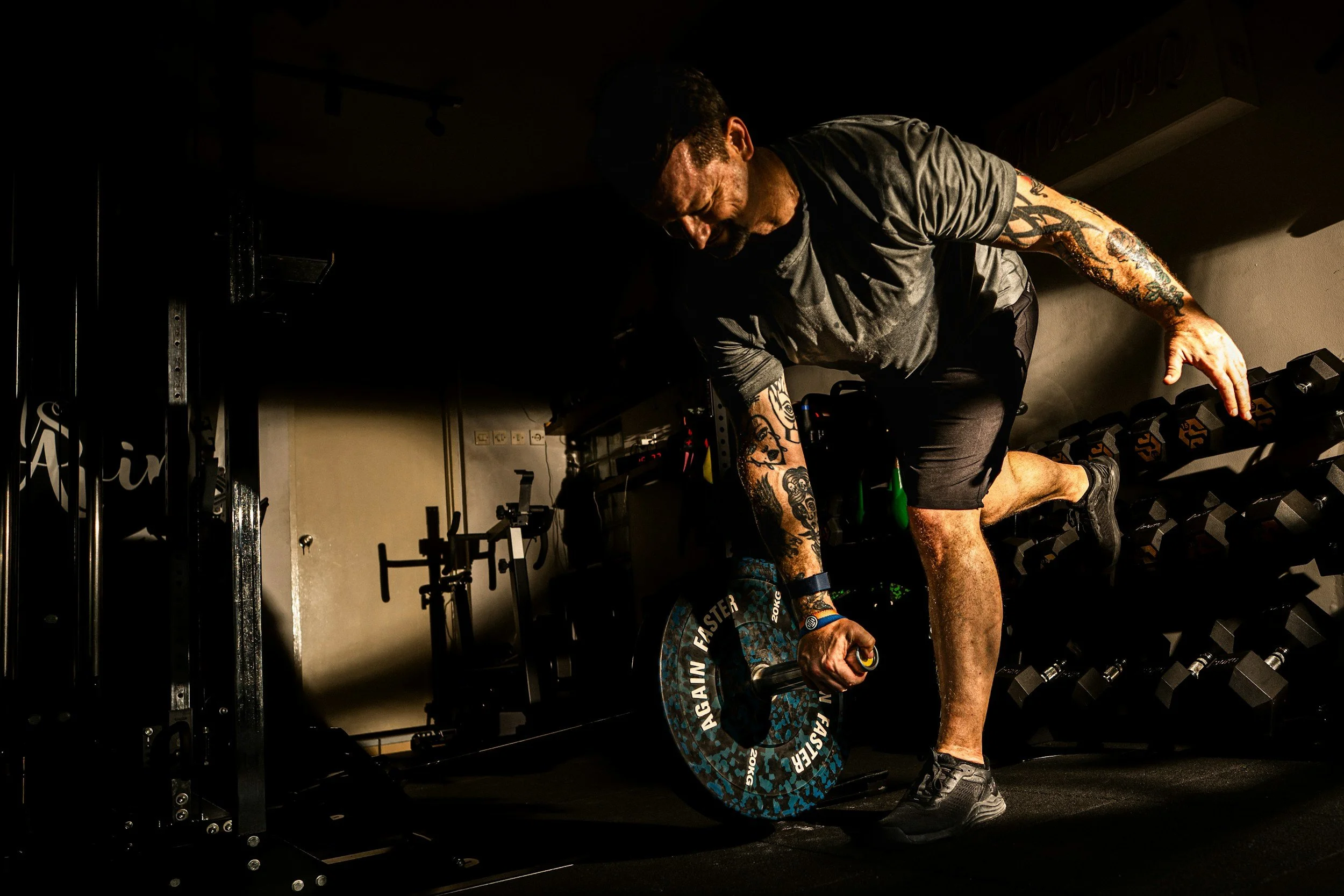 A man with tattoos on his arms and wearing athletic clothing is performing a deadlift with a barbell in a gym.