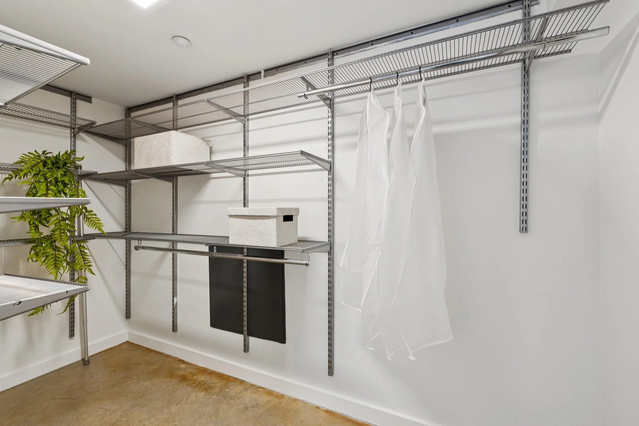 An empty storage room with metal wire shelving units, a box, a black door or panel, and hanging plastic garment covers.