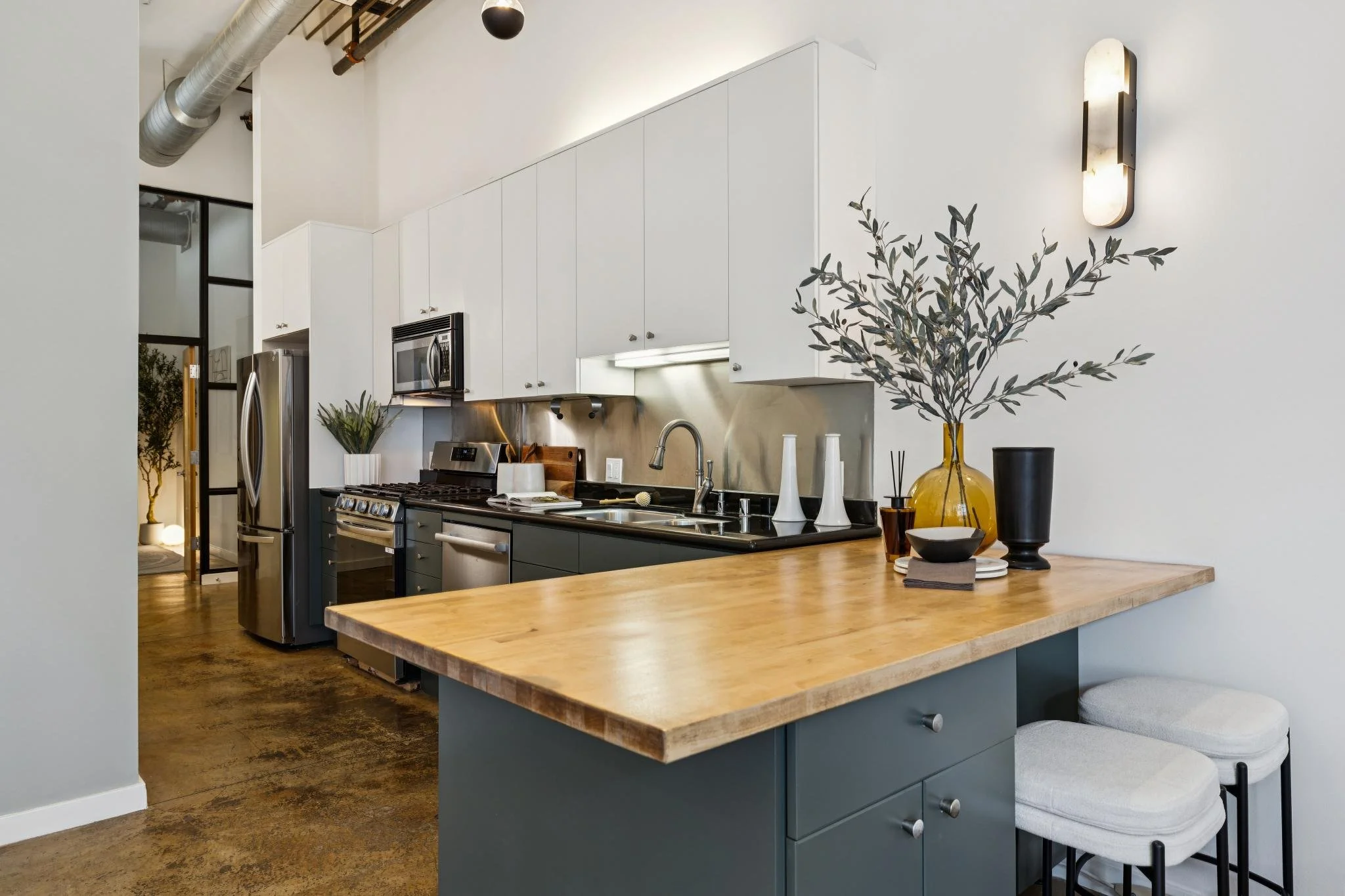 Modern kitchen with white upper cabinets, stainless steel appliances, a wooden island, and decorative vases and plants on the countertop.