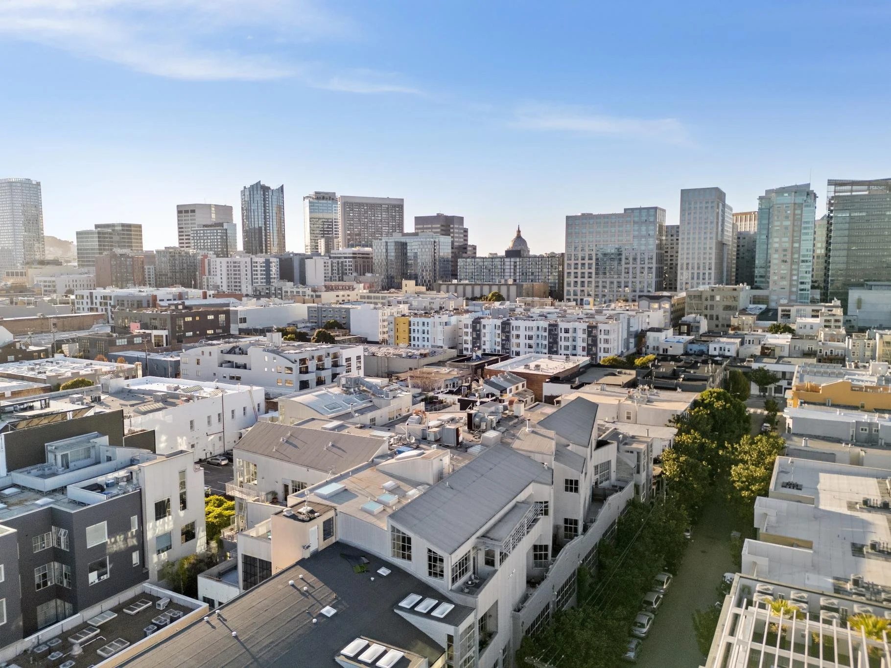 A city skyline featuring a mix of tall modern skyscrapers and shorter residential buildings, with a partly cloudy sky above.